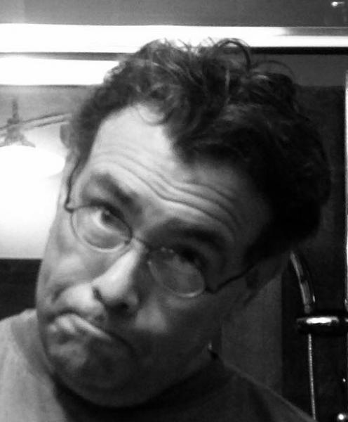 Man with glasses making a playful face, head tilted, in black and white.