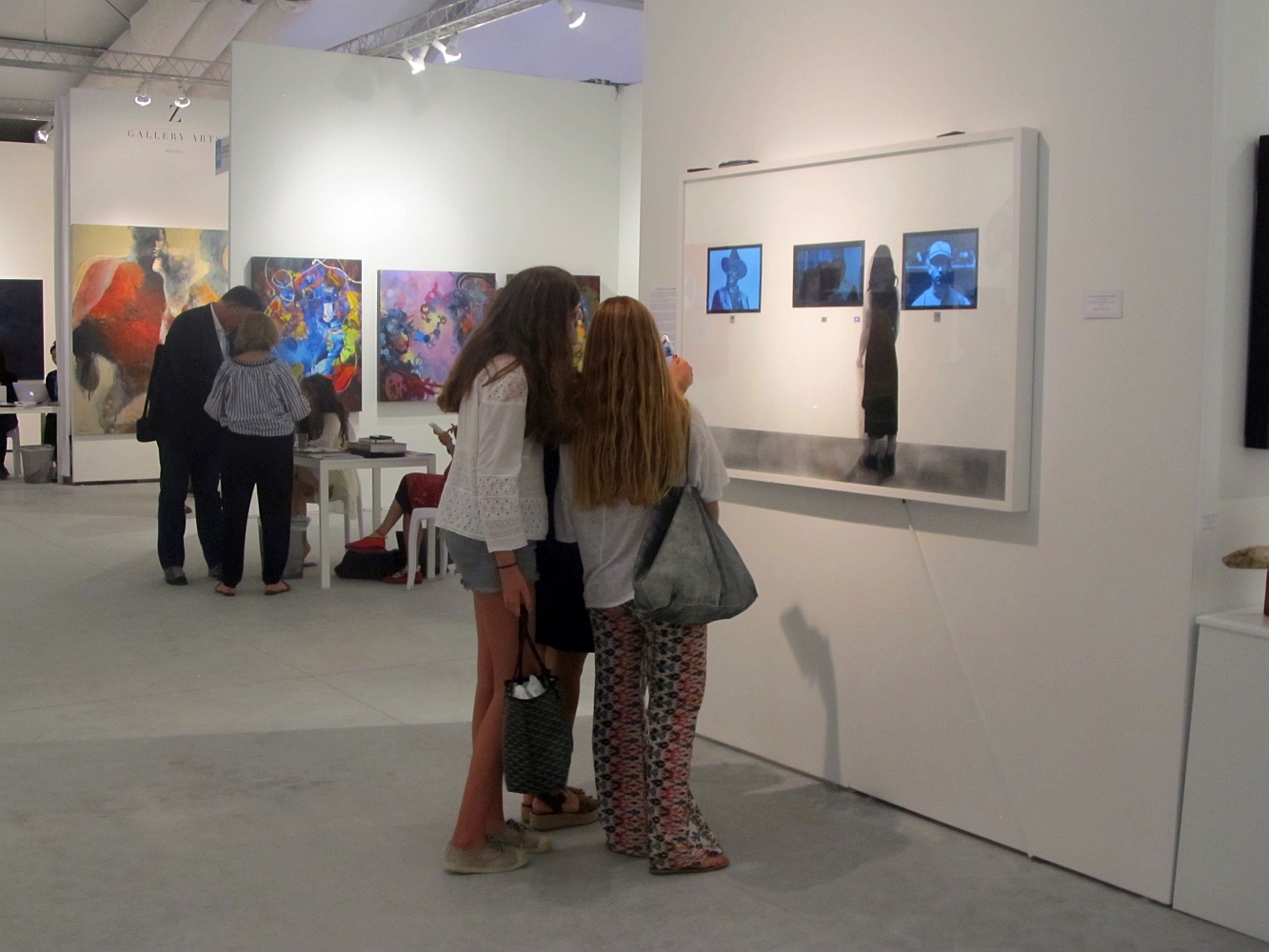 People viewing artwork in an art gallery with colorful paintings on the wall.