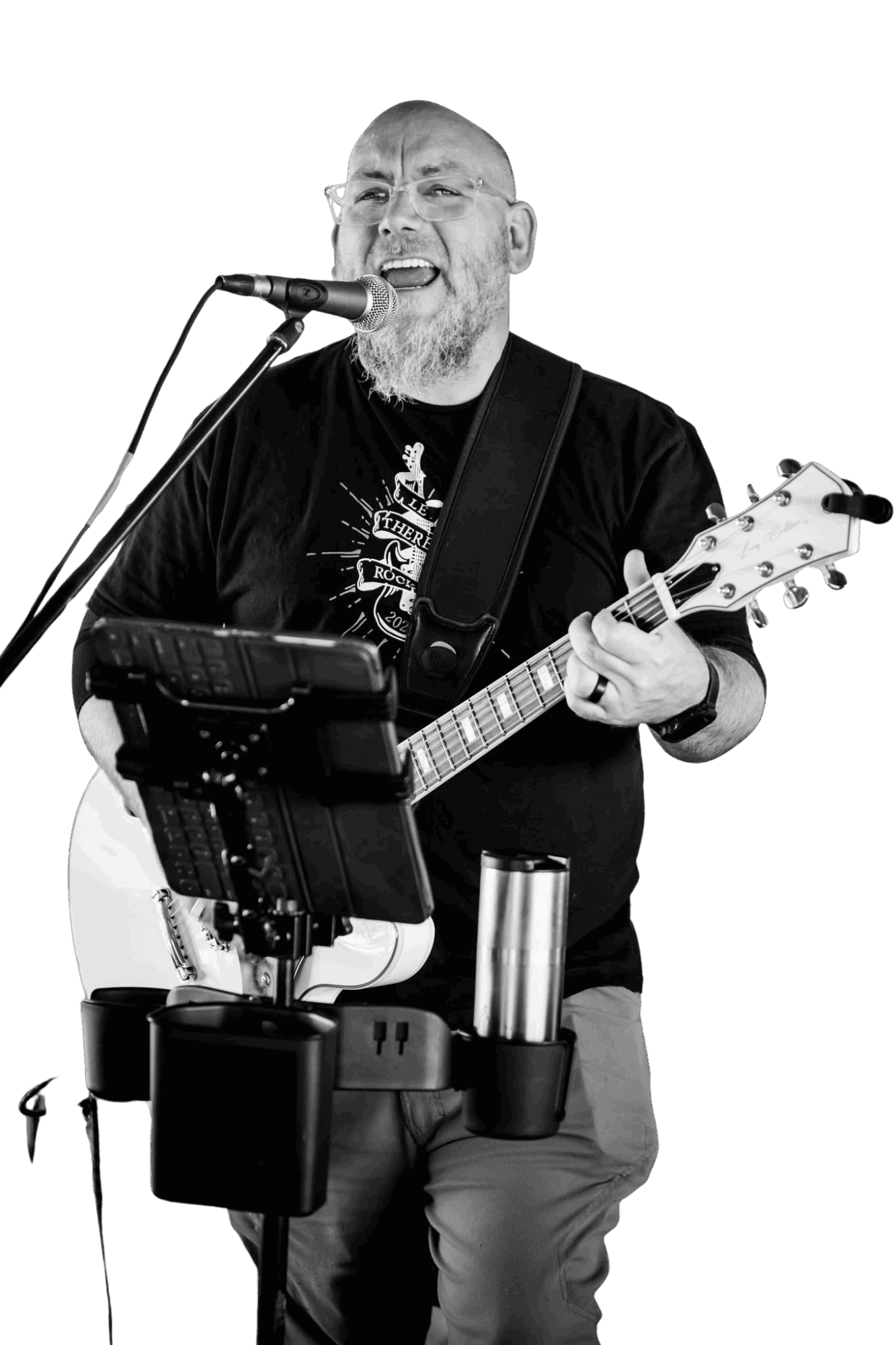Man singing into microphone while playing guitar, with music stand and equipment in front, against a black background.