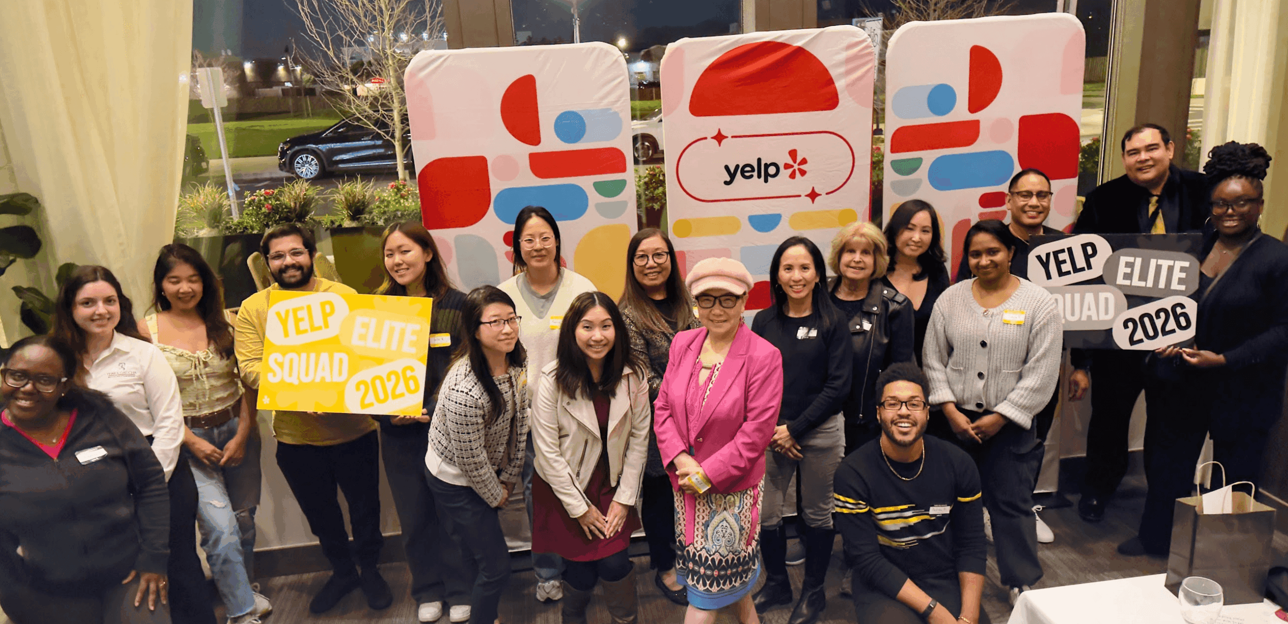Group of people standing outside with Yelp banners and signs, smiling for a photo.