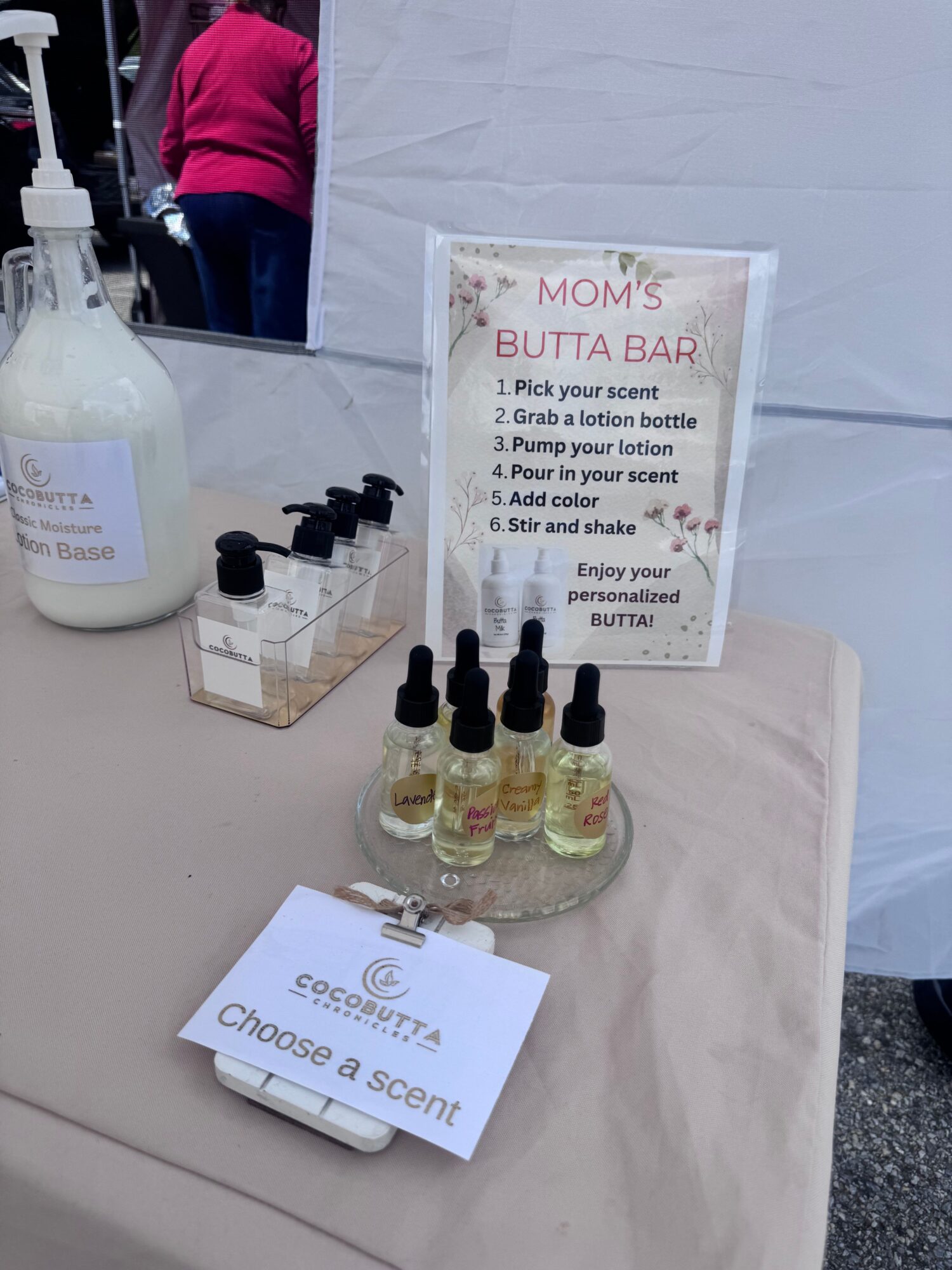 Display of small bottles with droppers, a sign about a mom's boutique bar, and a scent sample card on a table.
