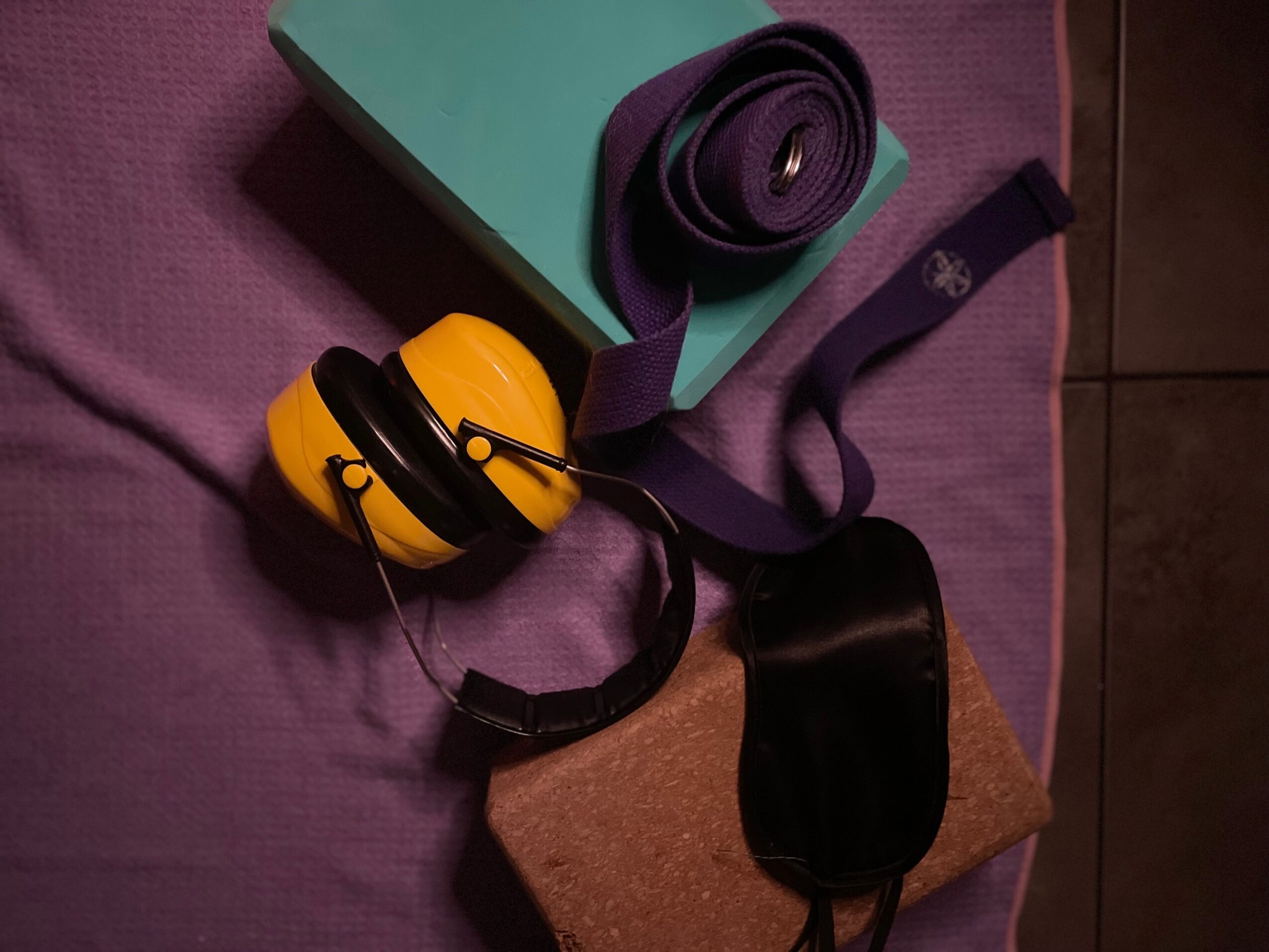 Headphones, a rolled strap, and a black pouch on a purple surface with a teal box nearby.