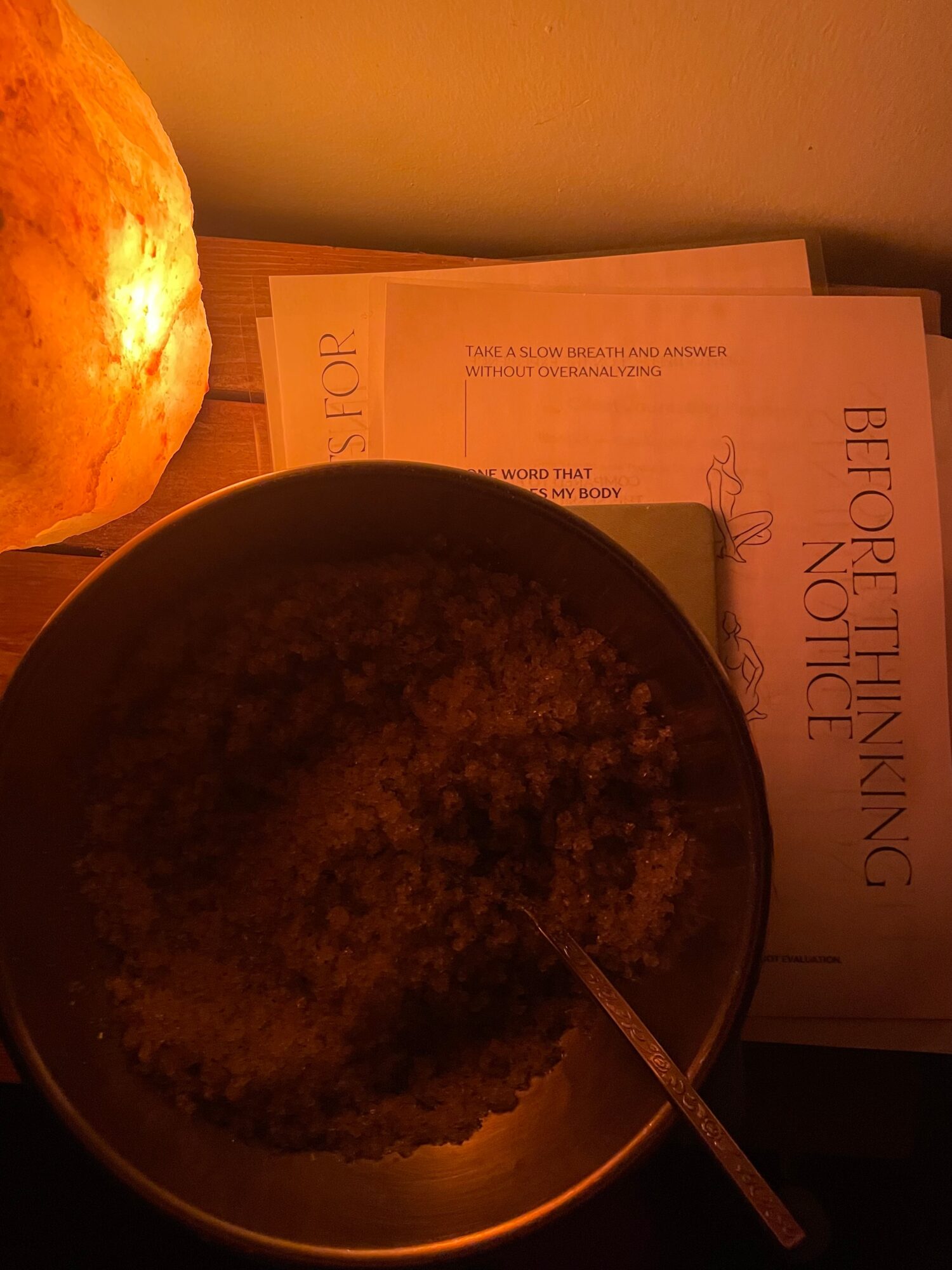 A bowl with a spoon, papers, and a pumpkin on a wooden surface in warm lighting.