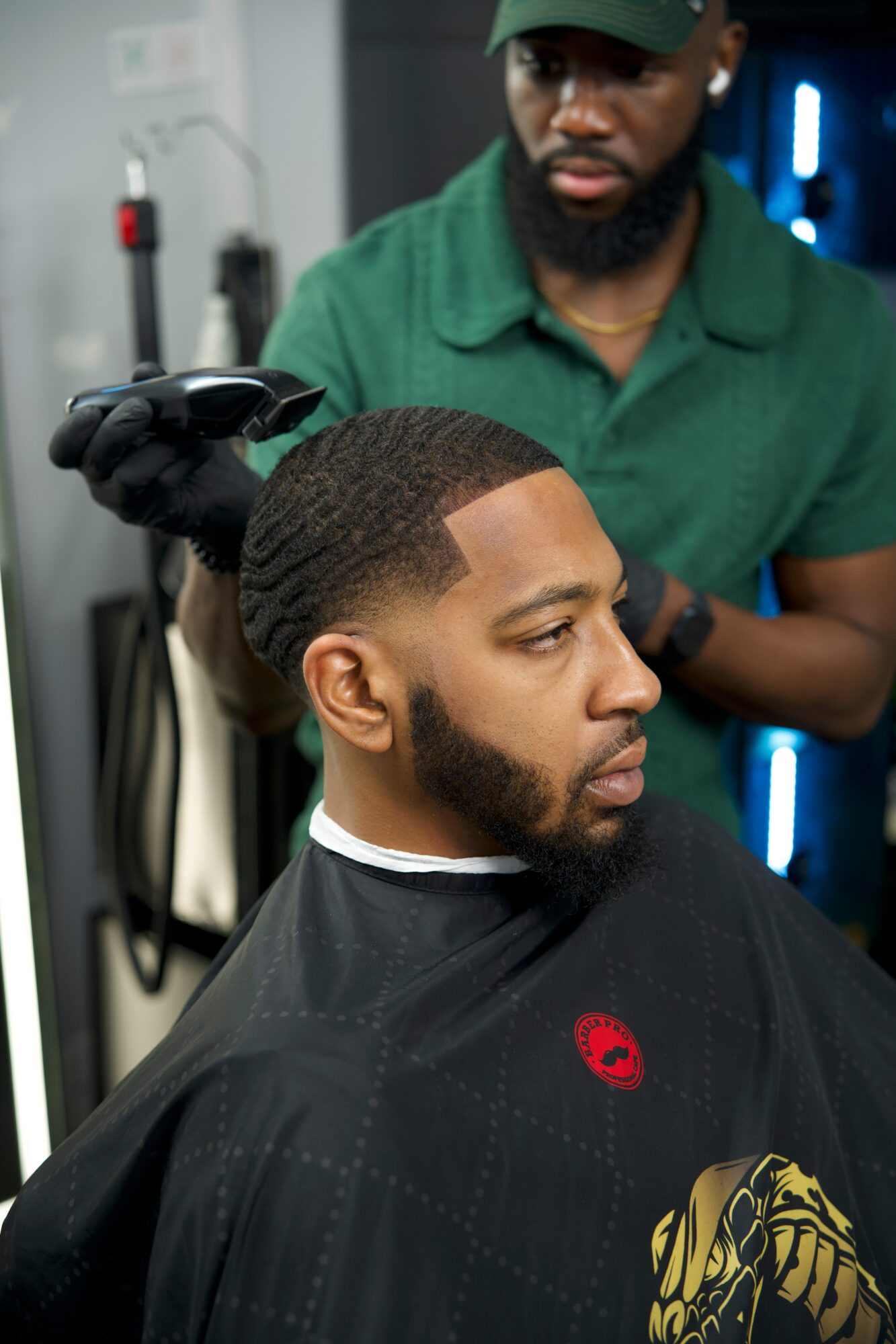 Barber trims a man's hair in a salon, with tools and equipment visible in the background.