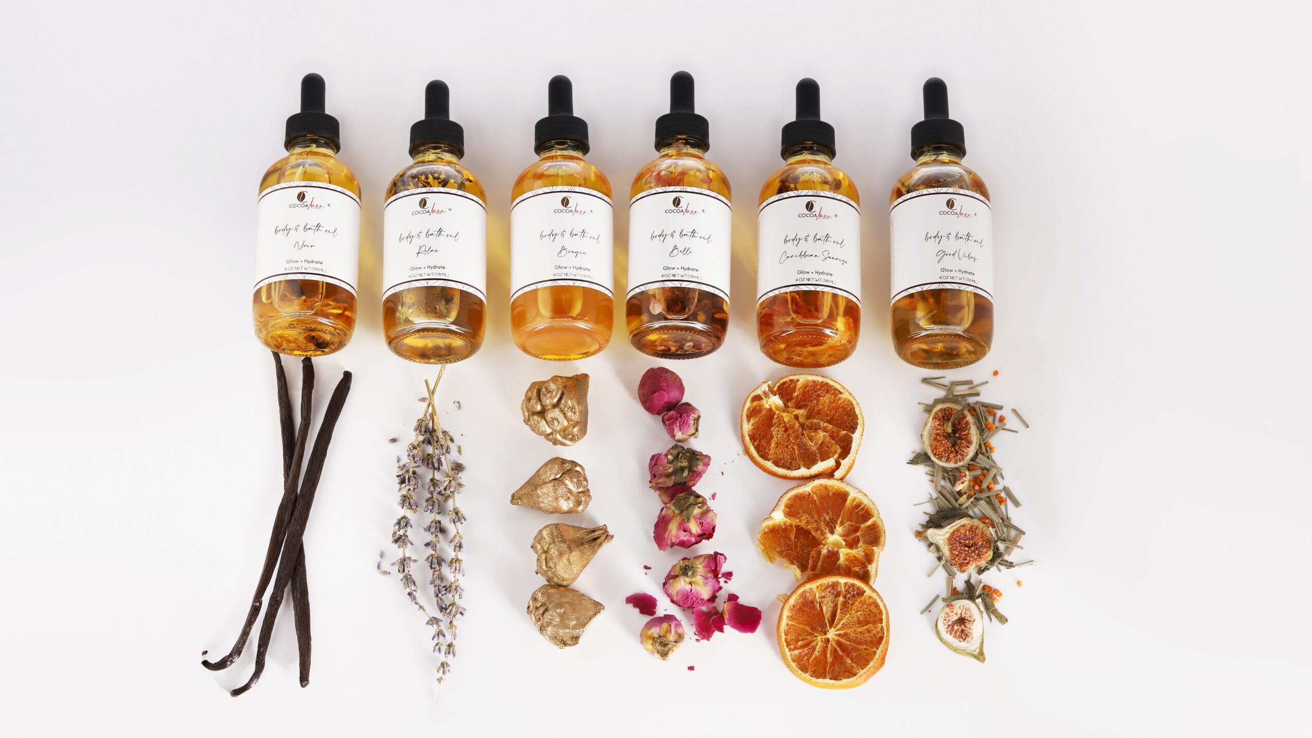 Six dropper bottles with liquids, dried herbs, crystals, dried orange slices, and flowers arranged on a white background.