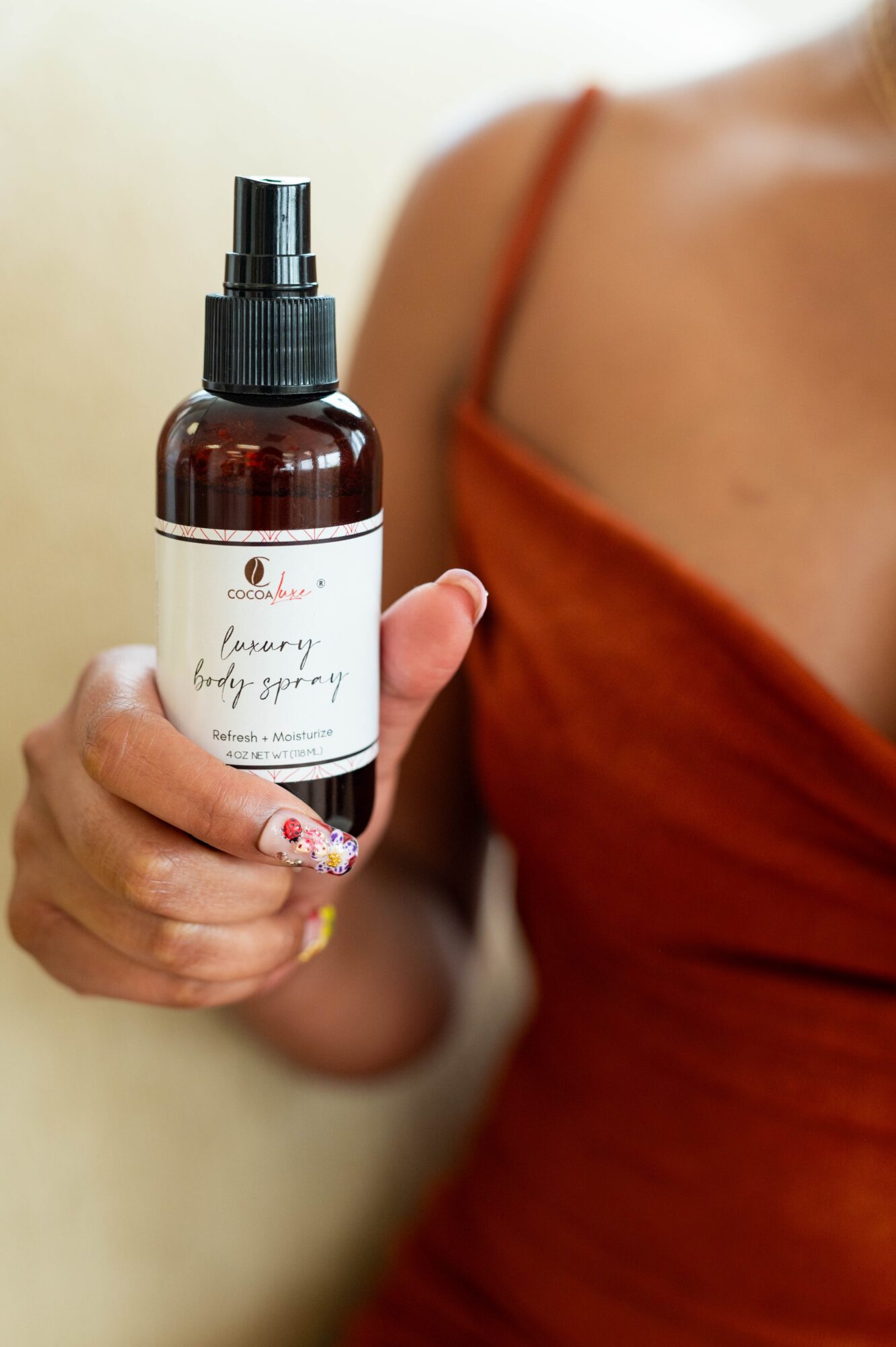 Person holding a brown spray bottle with a white label, wearing an orange top, against a light background.