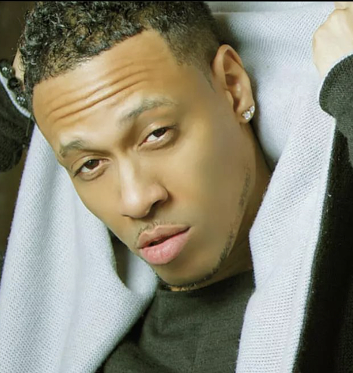 Close-up of a person with short curly hair, earrings, and a serious expression, lying on a light-colored surface.