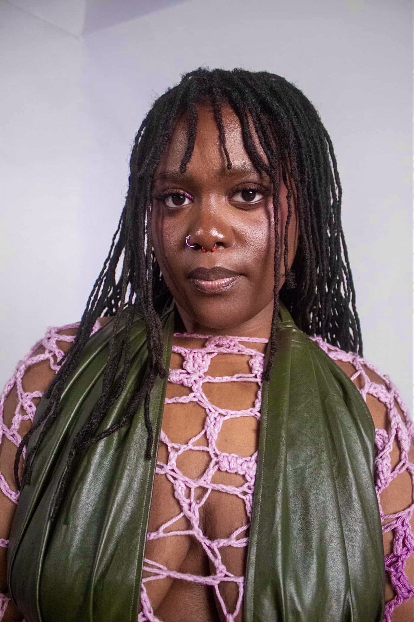 Woman with dreadlocks wearing a pink crochet top and green vest, looking at the camera.