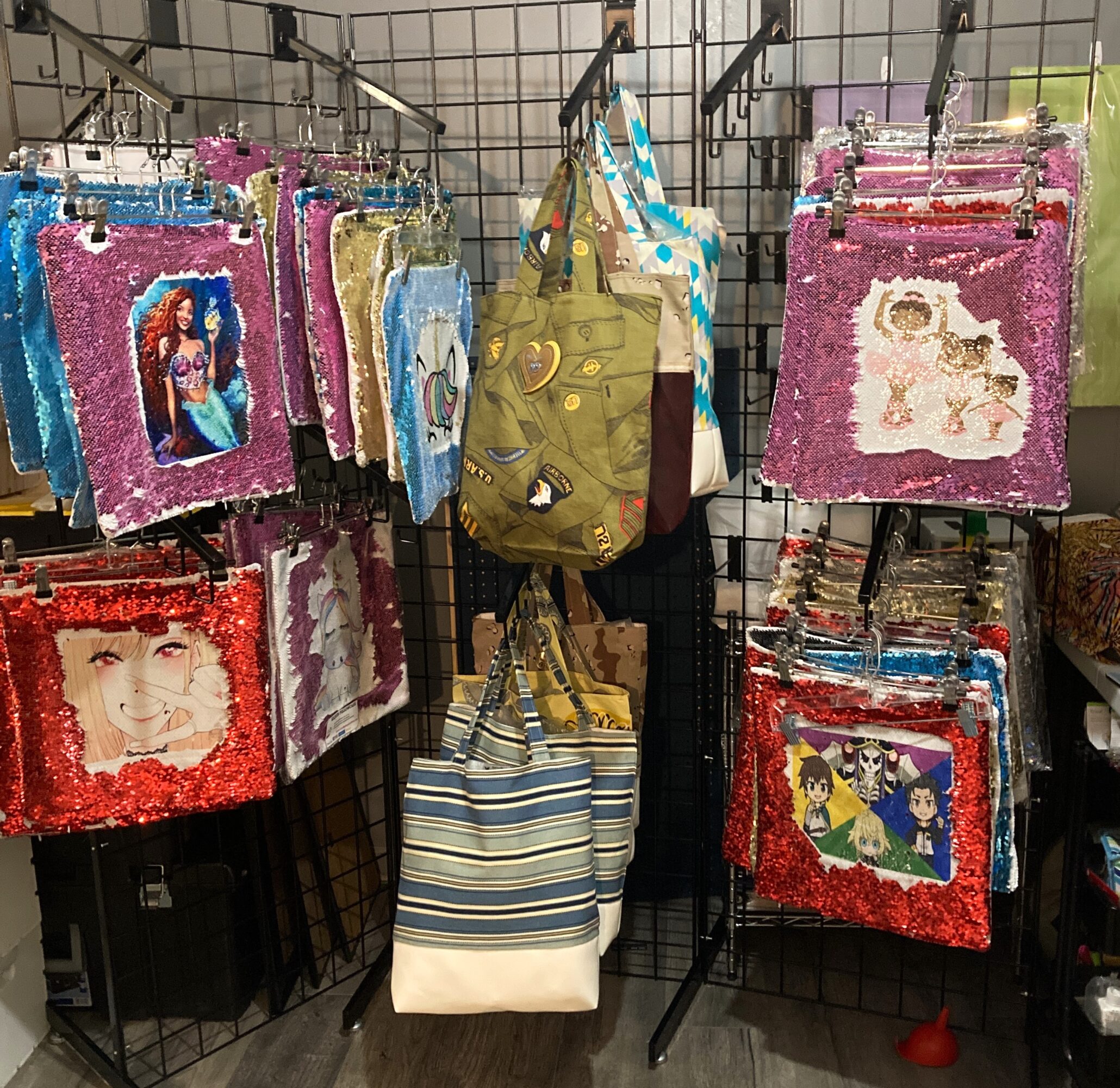Display of colorful sequined bags with cartoon characters, hanging on a black grid wall, with striped and solid bags in the center.