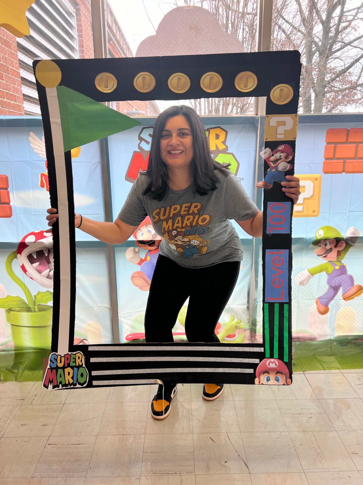 Woman standing inside a colorful cardboard frame at an indoor event, with a mural and window in the background.
