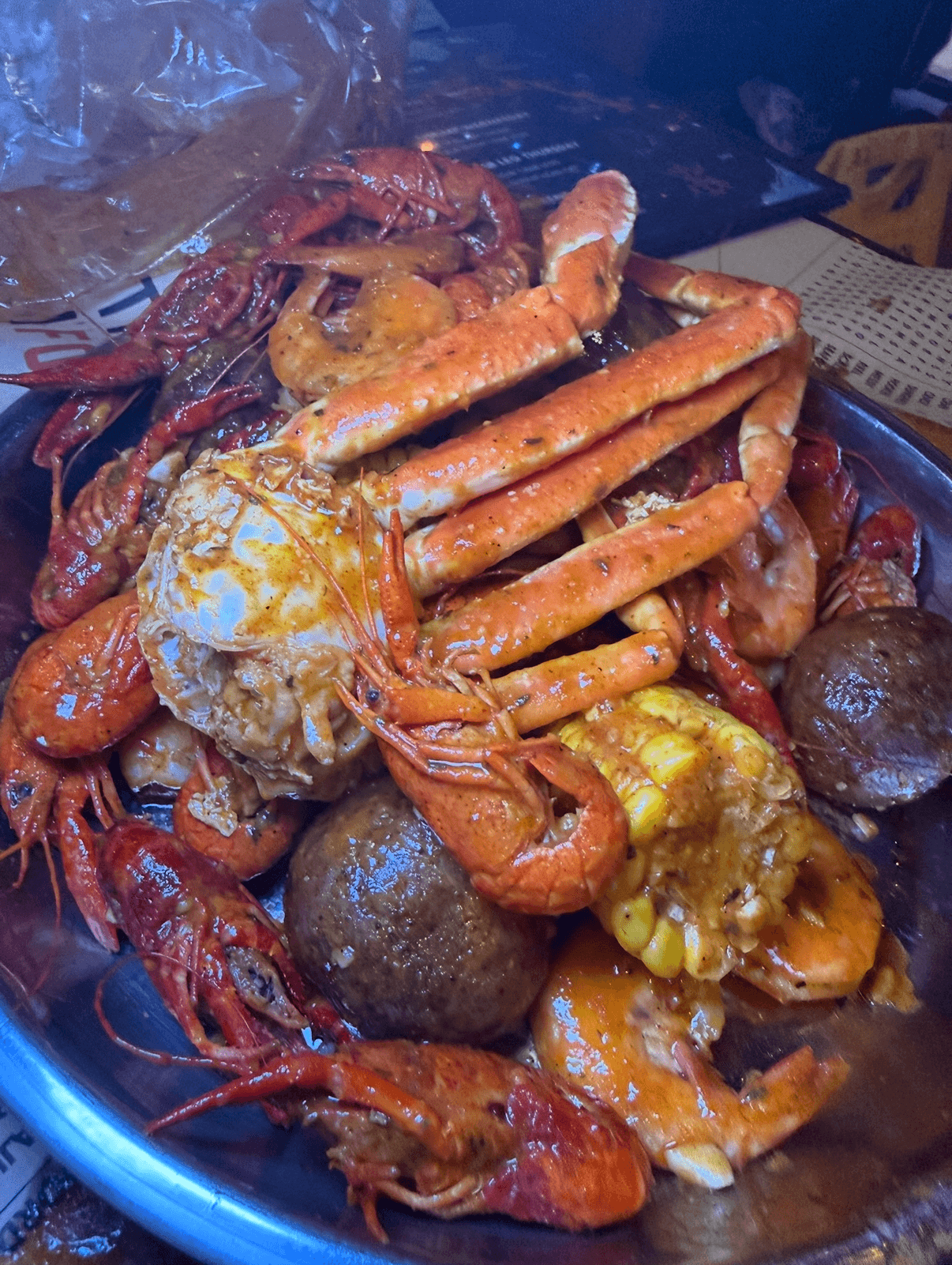 Seafood boil with lobster, crab, shrimp, potatoes, and corn in a bowl, with a plastic bag in the background.