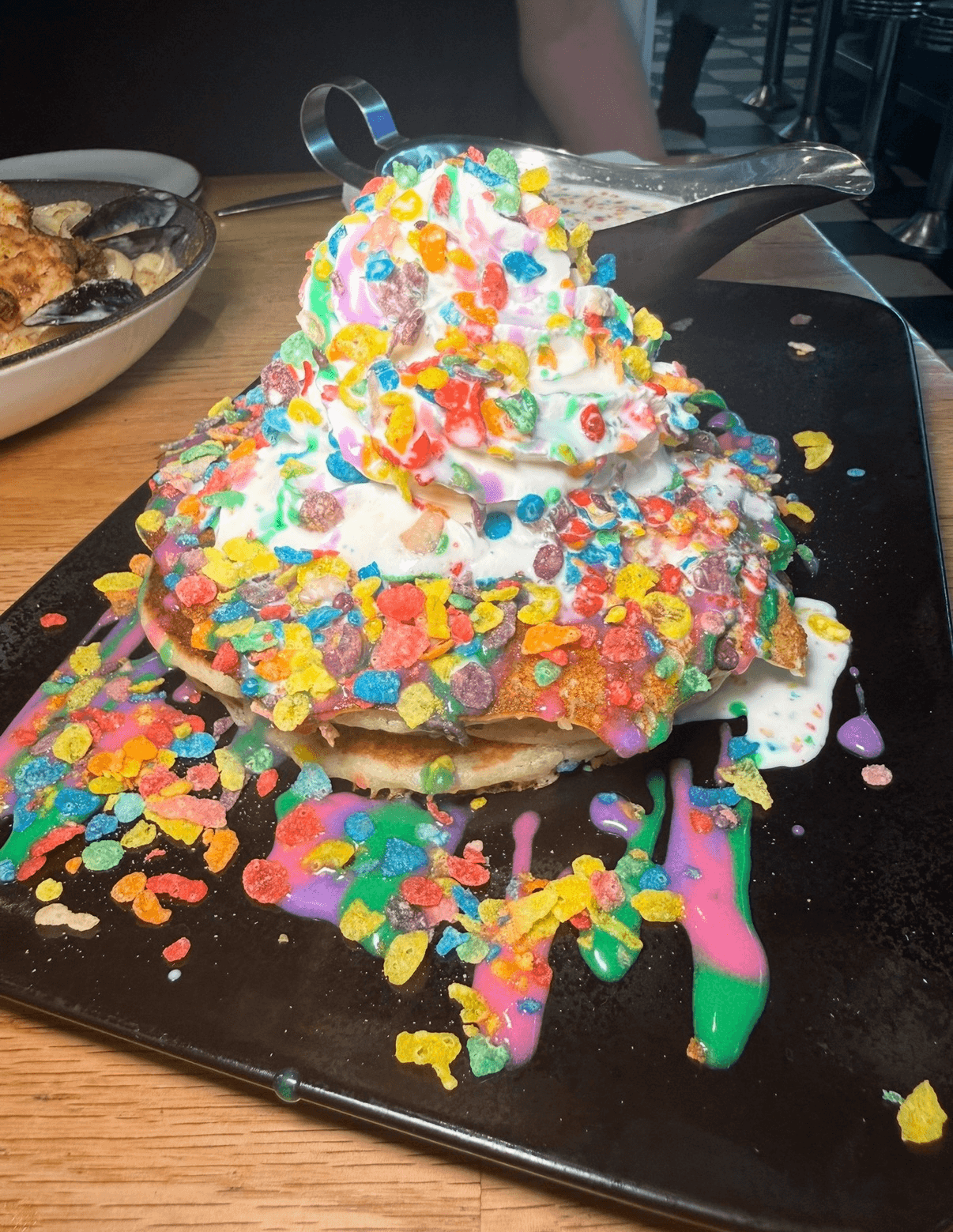 Colorful ice cream sundae with sprinkles and toppings on a black plate, on a wooden table.