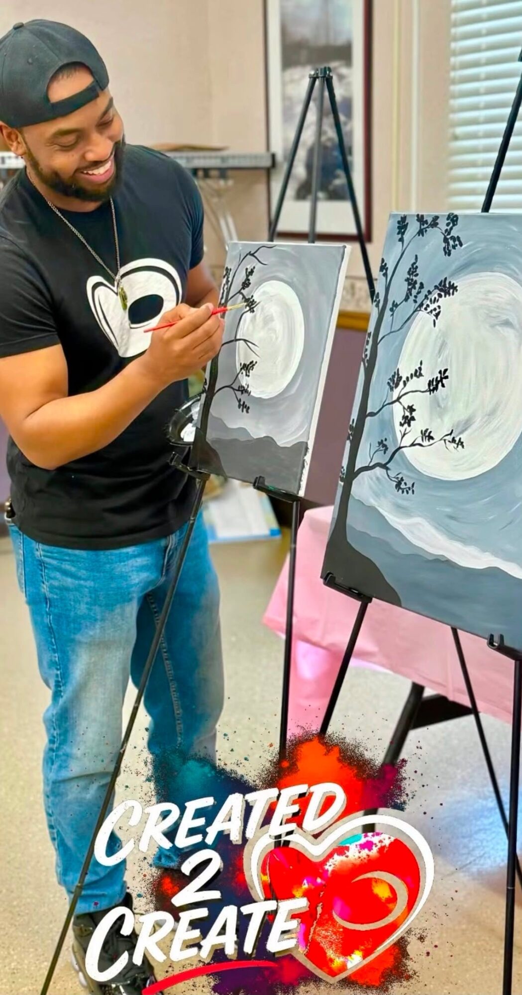 Person painting a landscape with a moon, trees, and water on an easel, smiling and holding a paintbrush.
