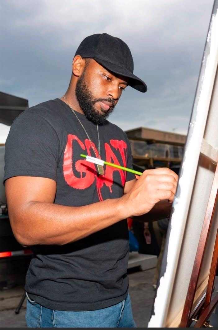 Man wearing a black cap and T-shirt painting on a canvas outdoors under cloudy sky