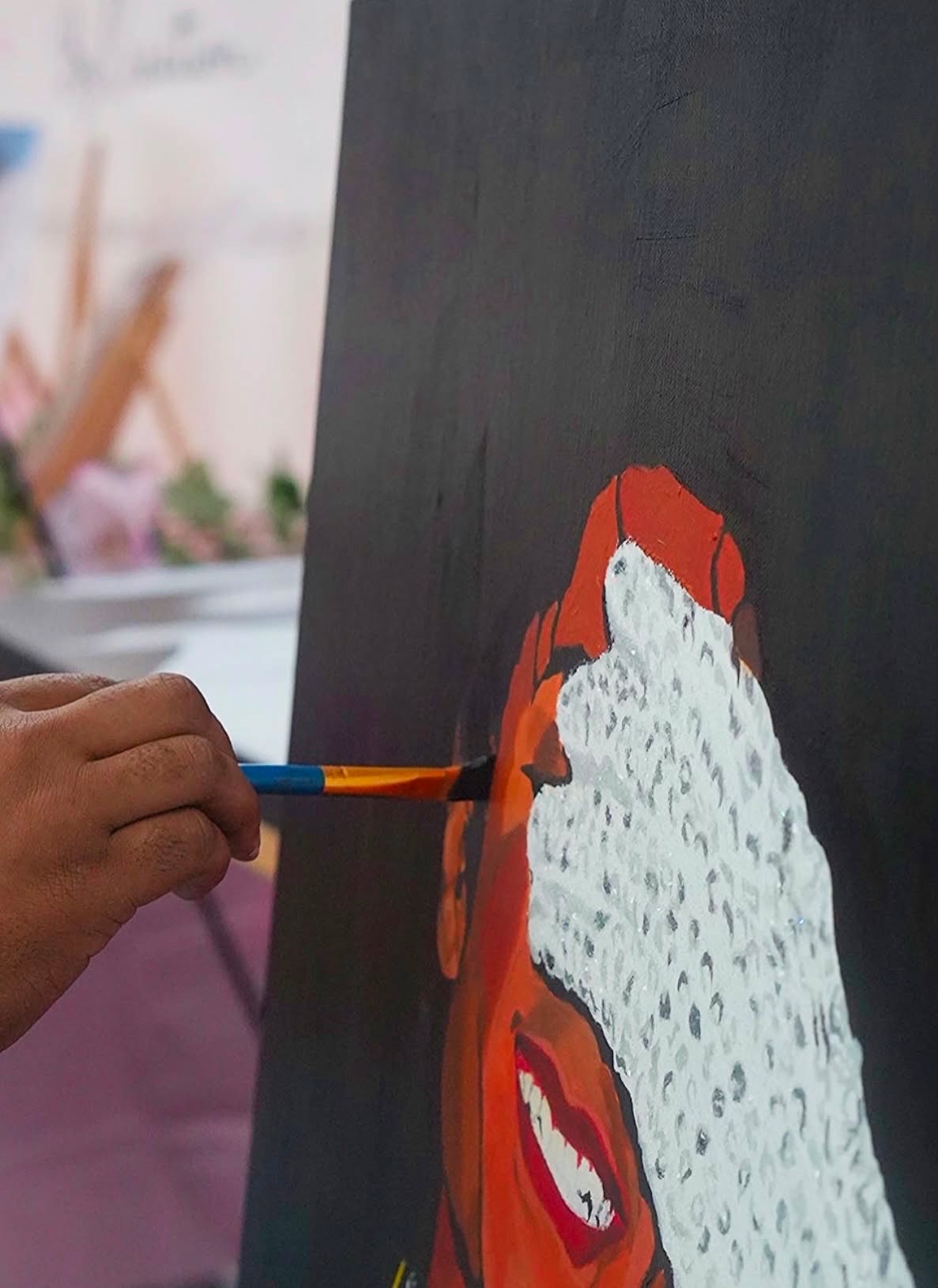Person painting a face with red, white, and black colors on a dark background, holding a paintbrush in hand.