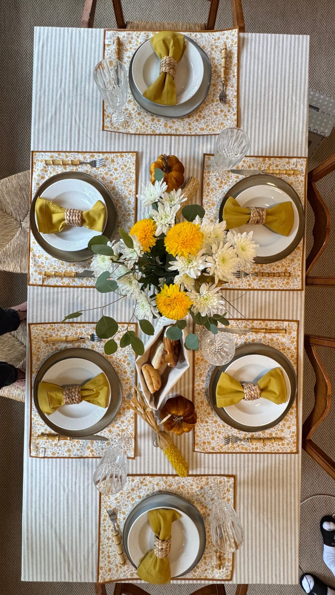 Table setting with six plates, gold utensils, floral centerpiece, and decorative napkins, viewed from above.