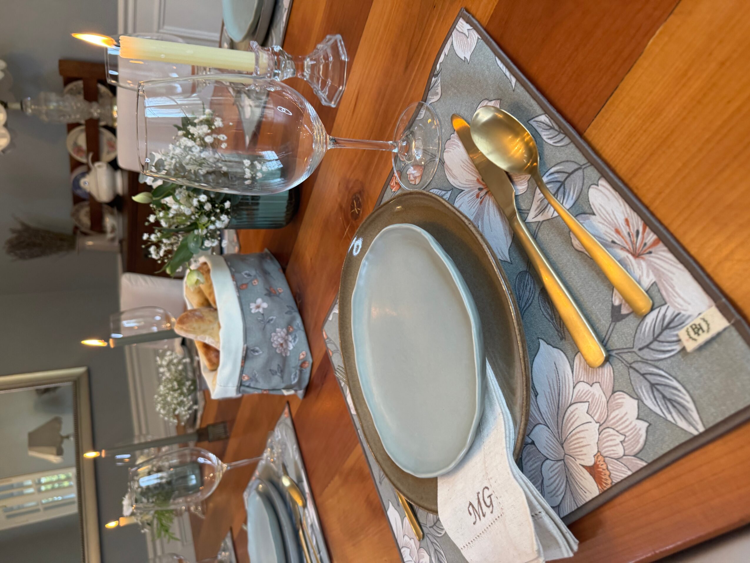Empty plate on a floral placemat with a yellow-handled spoon and knife, set on a wooden table with glasses and a tissue box.