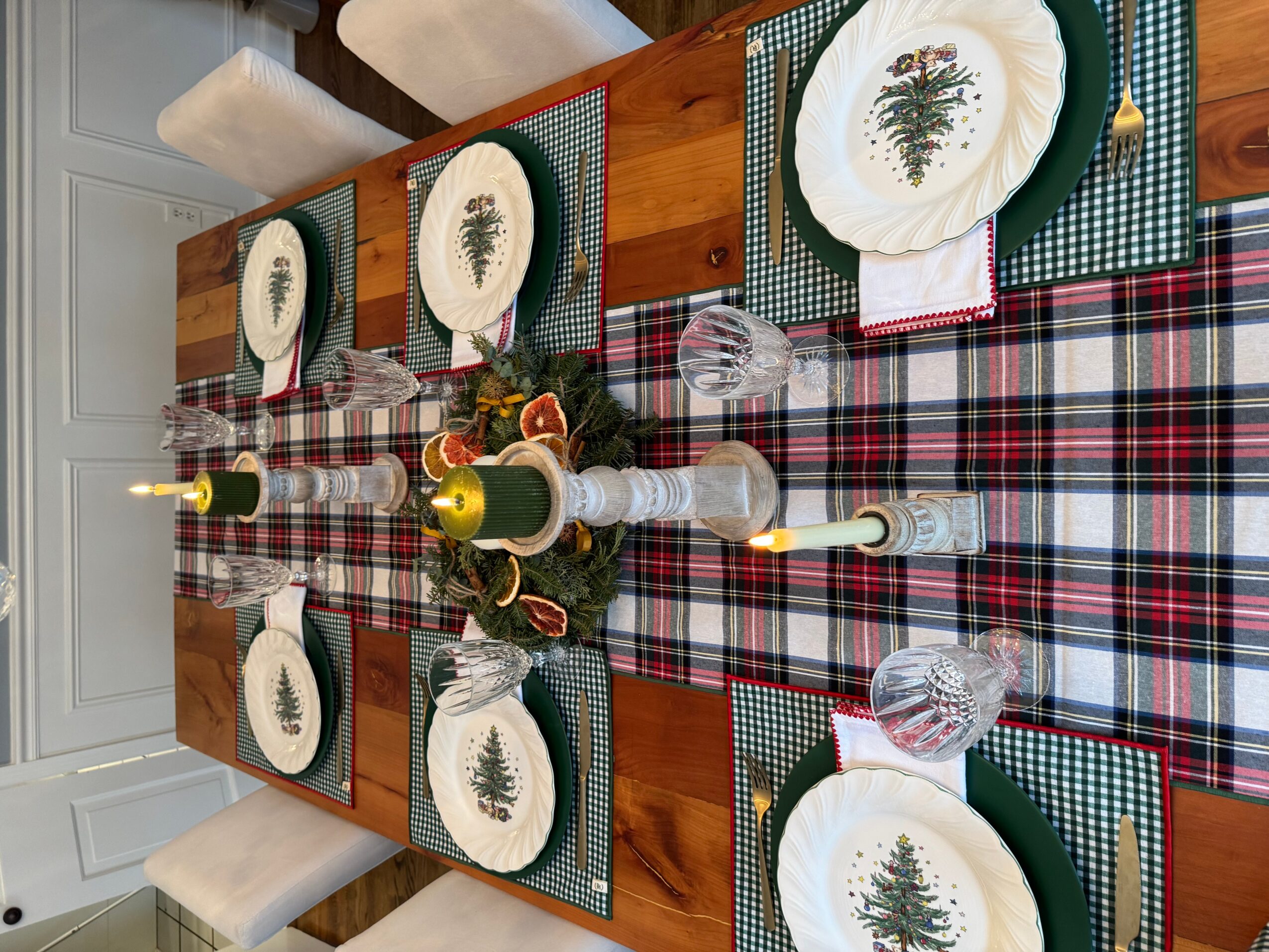 A festive table setting with plates, glasses, candles, and a plaid table runner, decorated for a holiday meal.