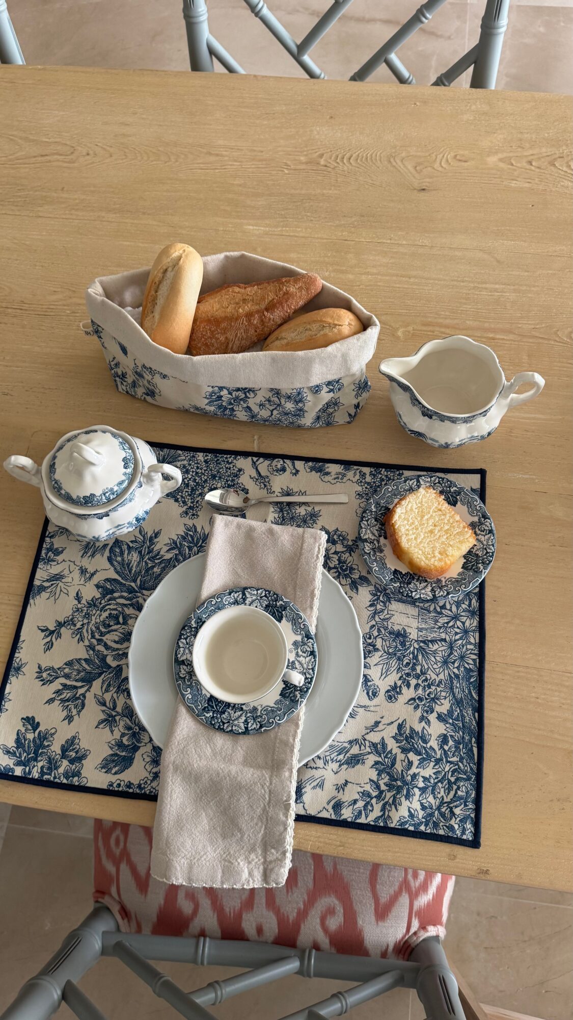 Table with bread, butter, and cream pitcher on a blue and white patterned tray, with a small cake and a teapot.