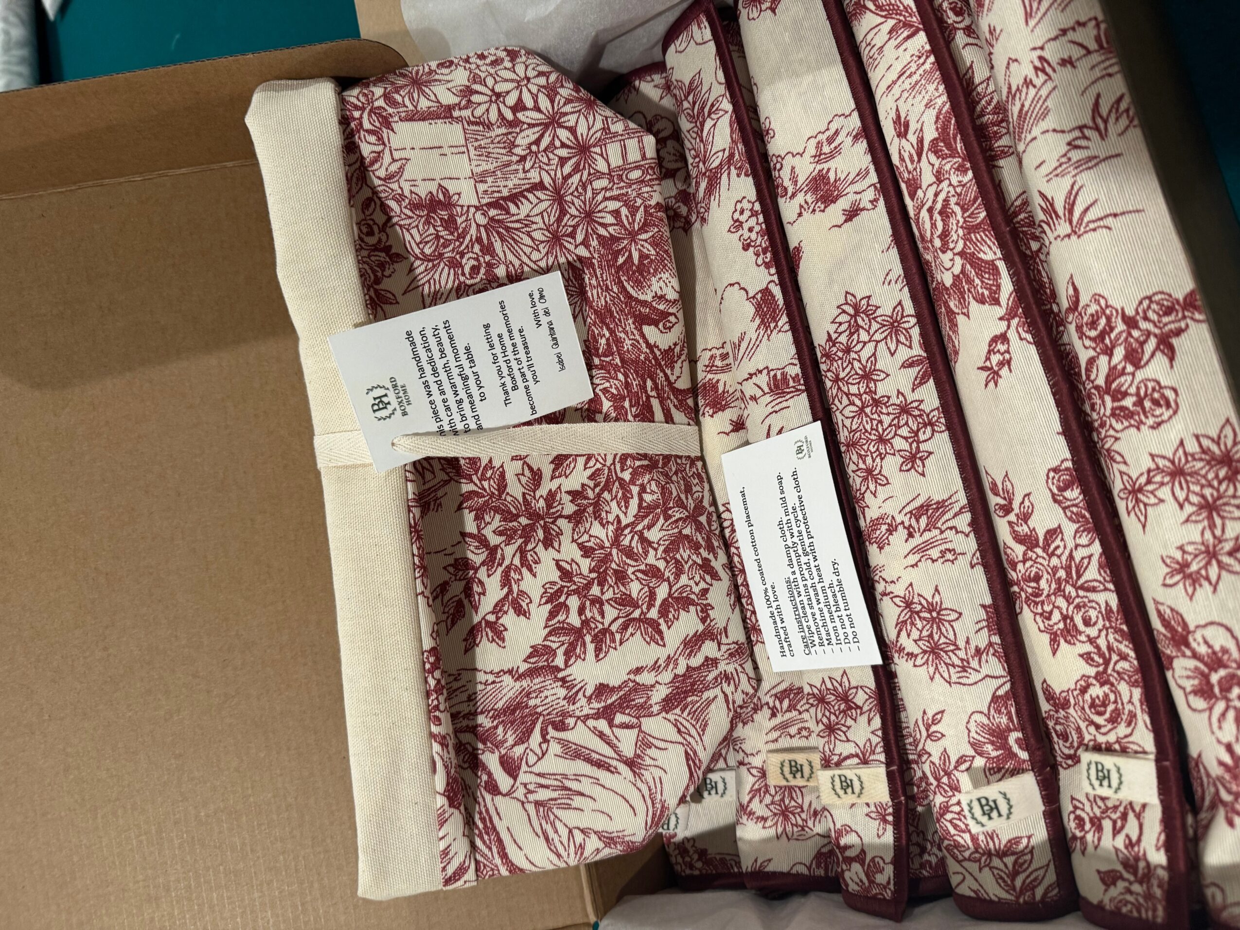 Four stacked mattresses with red and white floral patterns, tags attached, on a cardboard surface.