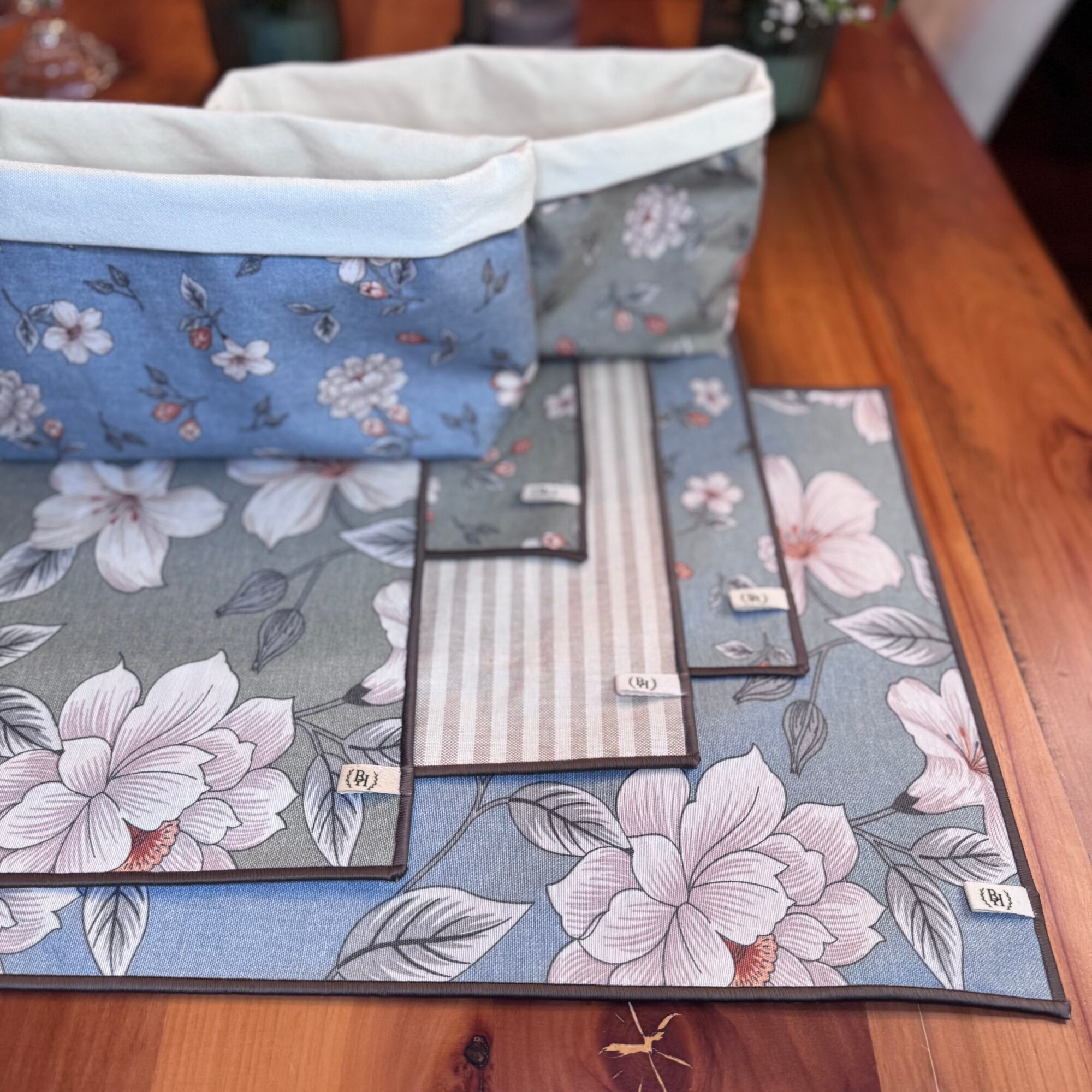 Two fabric storage baskets on a floral-patterned mat on a wooden surface, with fabric swatches nearby.