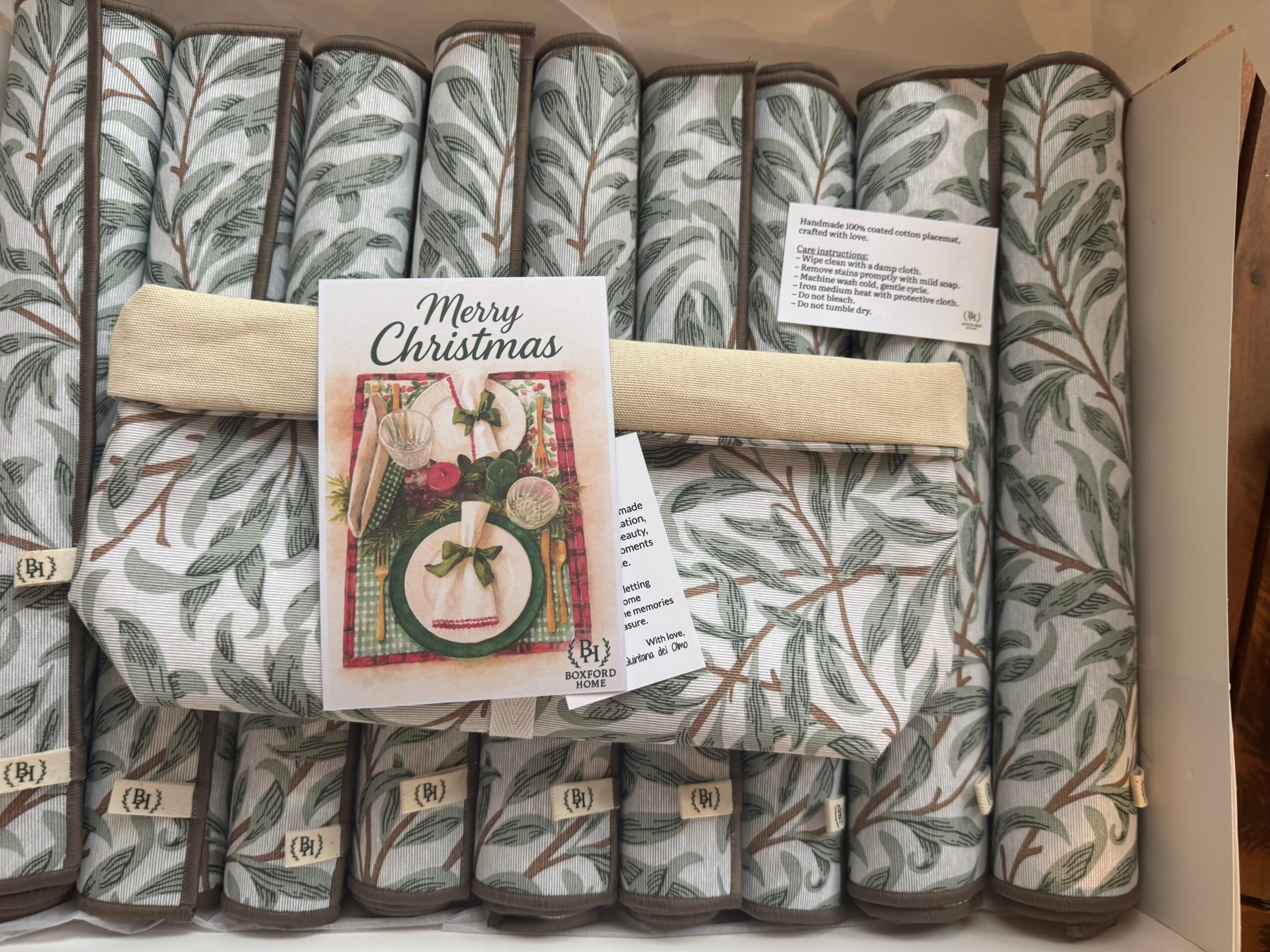 Set of rolled fabric or paper items with a Christmas card and a cream-colored ribbon on top, arranged in a row.