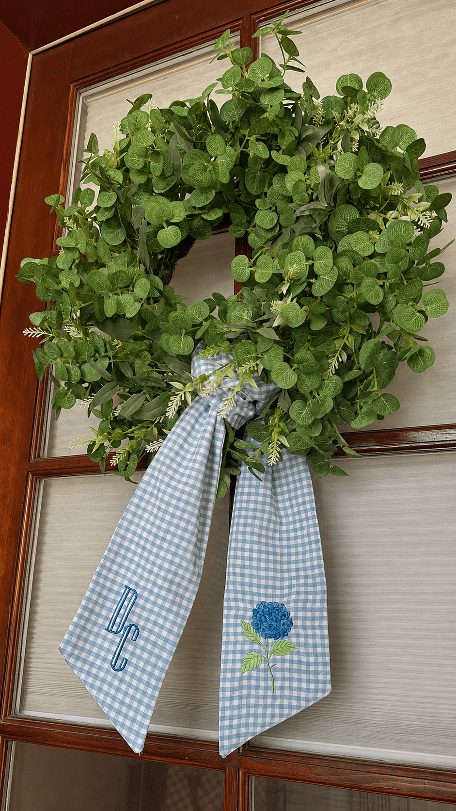 Green leafy plant with a blue checkered ribbon and embroidered flower, hanging on a door.