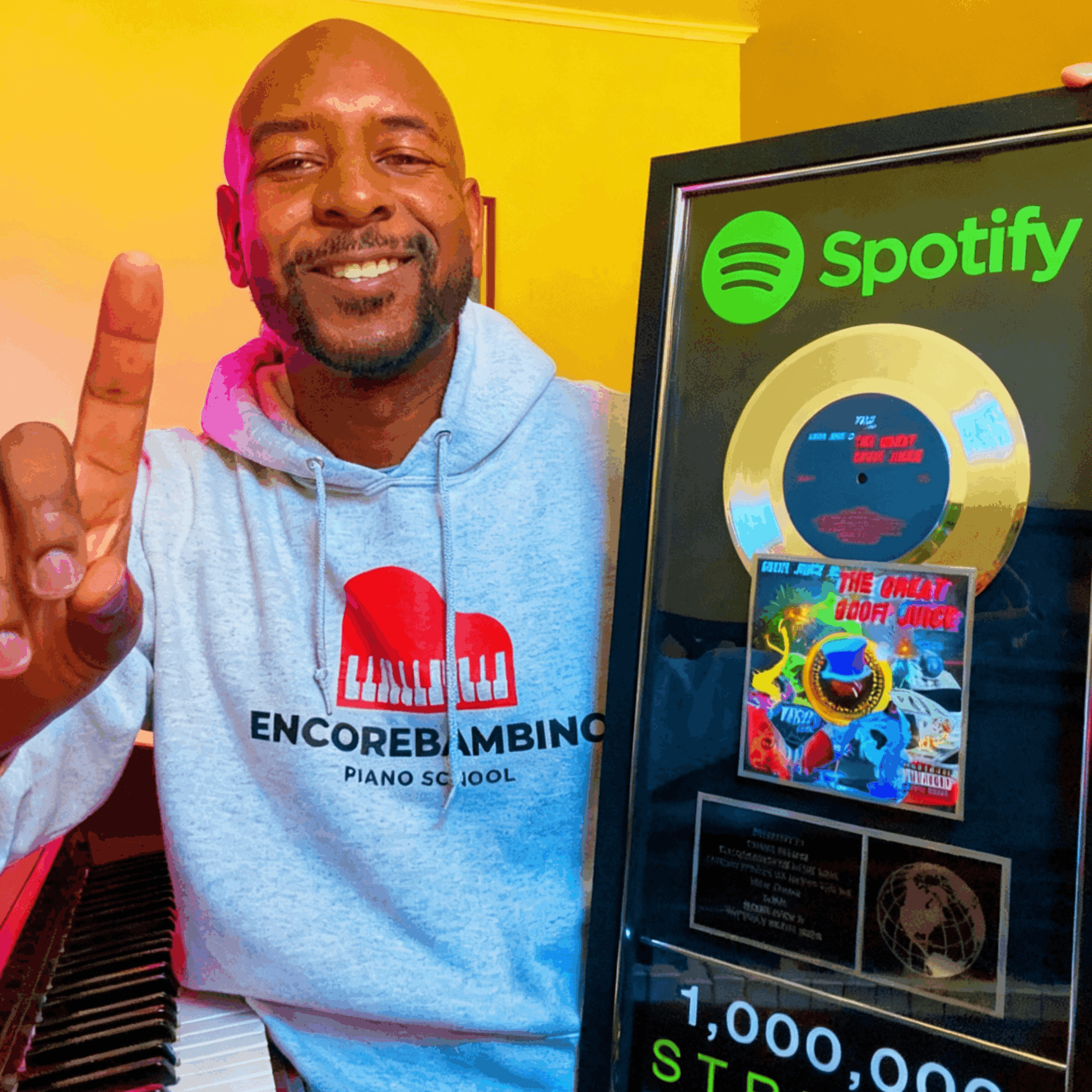 Smiling man in hoodie showing one finger next to a screen displaying a Spotify logo and a music album cover.
