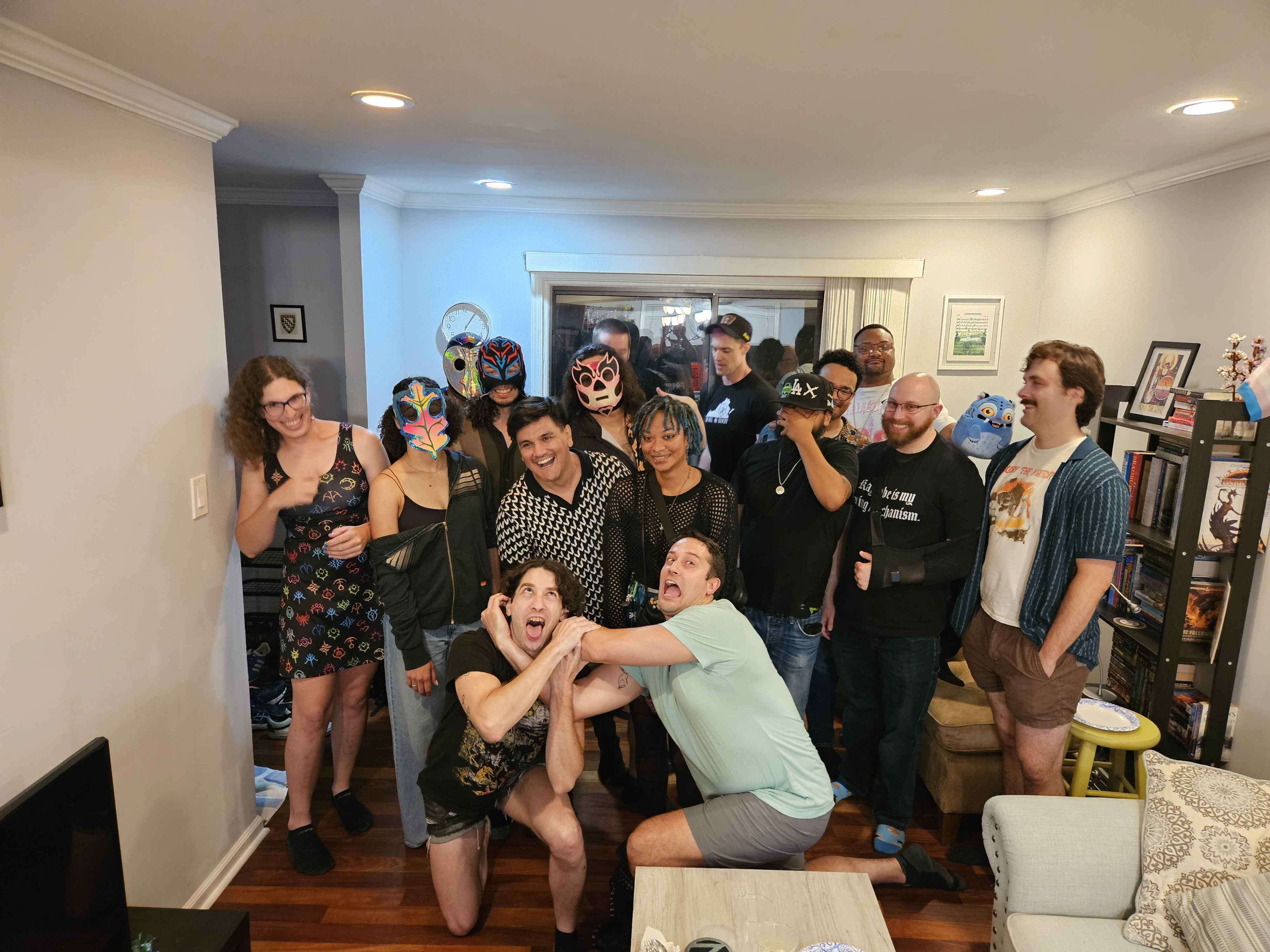 Group of people gathered in a living room, some wearing masks, smiling and posing for a photo, with furniture and decorations visible.