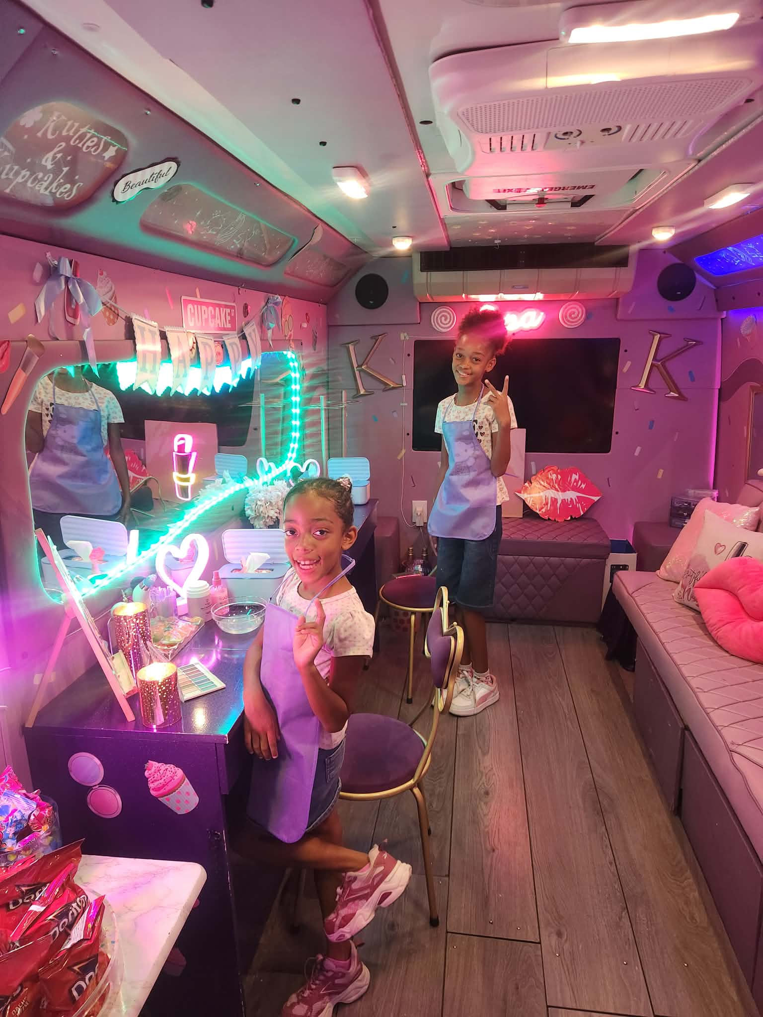 Two children in a decorated room with pink and blue lighting, one sitting and one standing, surrounded by party decorations.