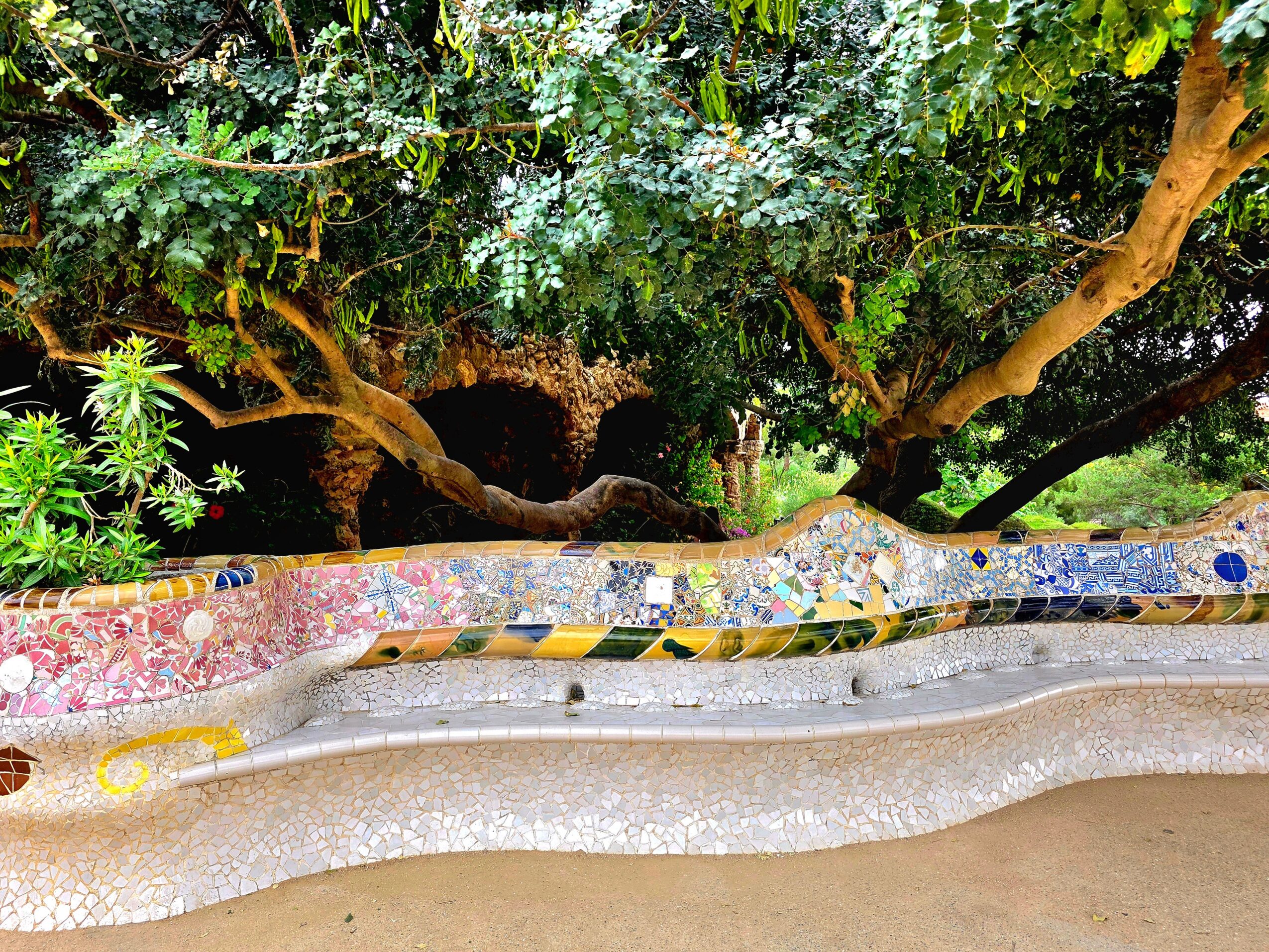 Colorful mosaic bench with trees and greenery in the background.
