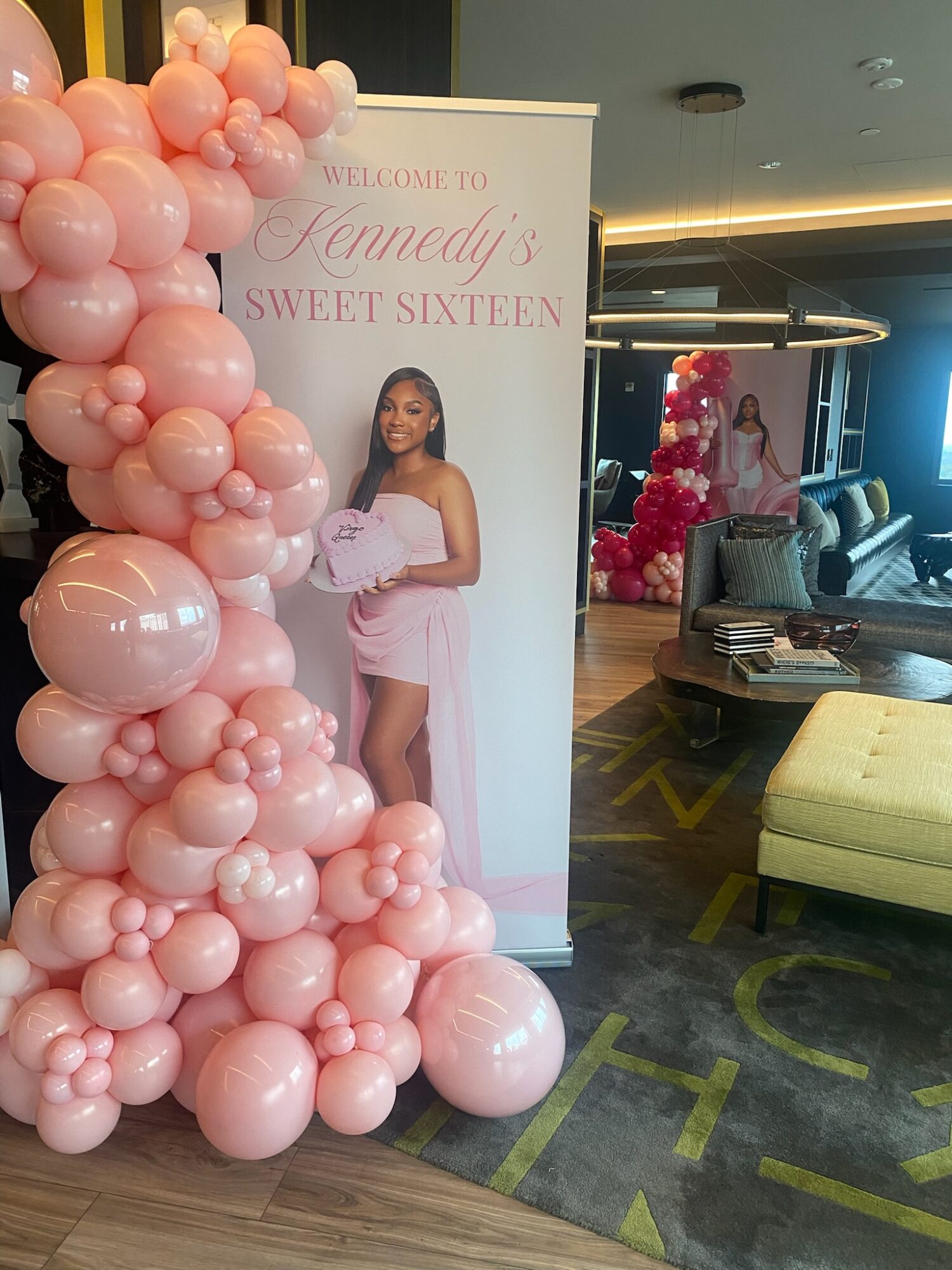 Party decoration with pink balloons and a banner for a sweet sixteen celebration, featuring a girl in a pink dress.