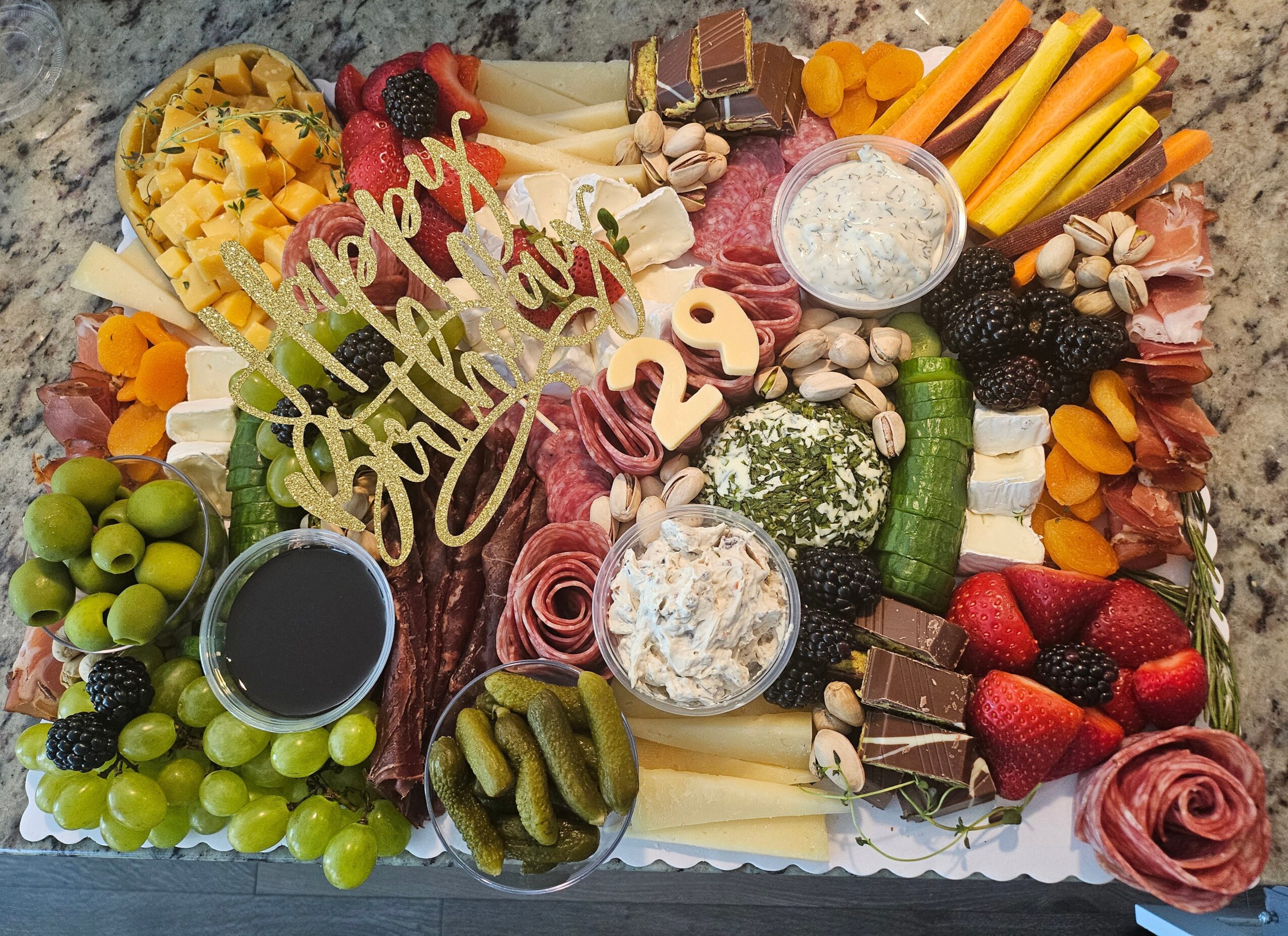 Assorted fruits, chocolates, cheeses, and snacks arranged on a platter with a decorative 'Happy Birthday' sign.