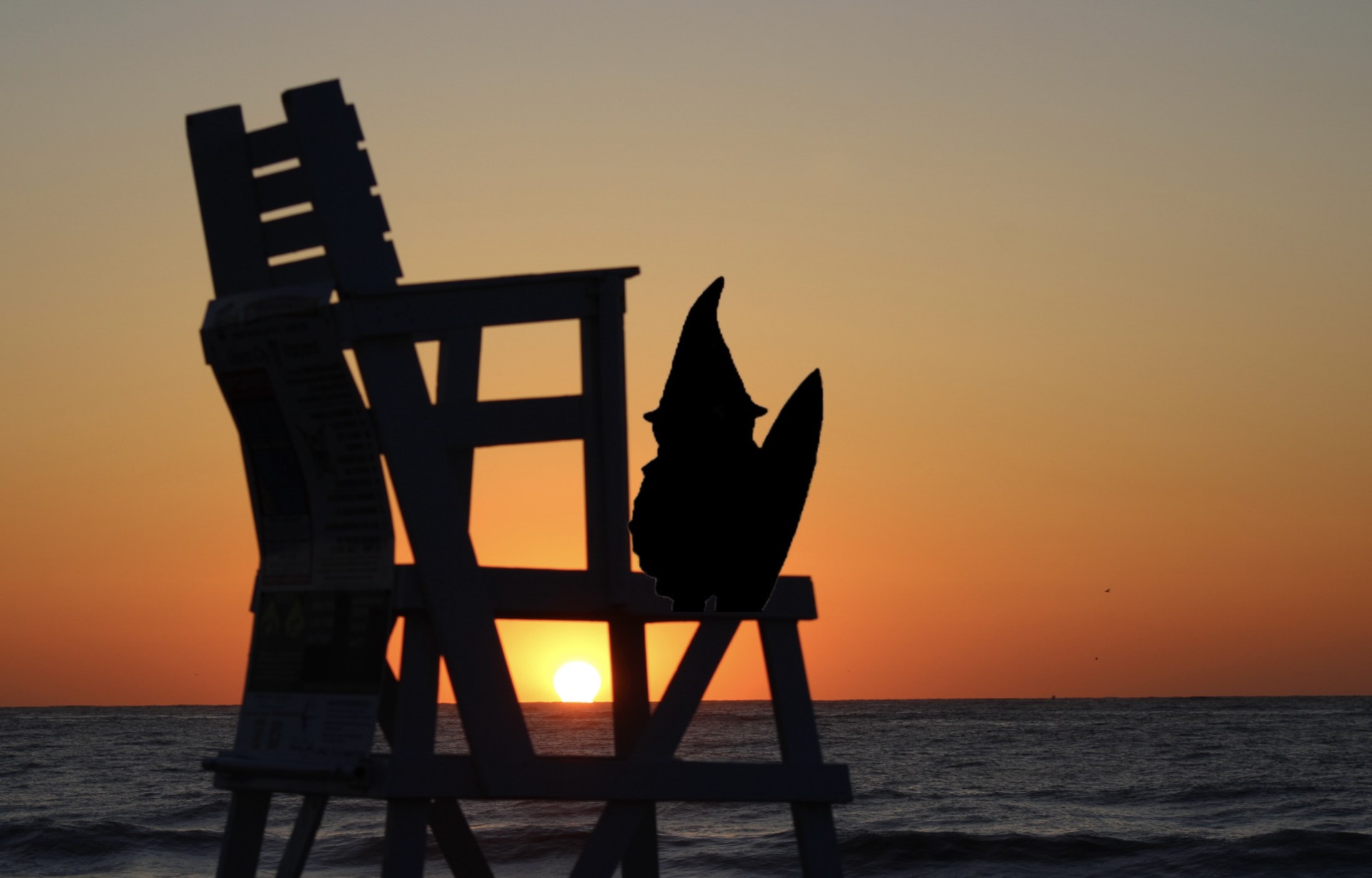 Silhouette of chairs on the beach at sunset with the sun near the horizon, ocean waves visible.