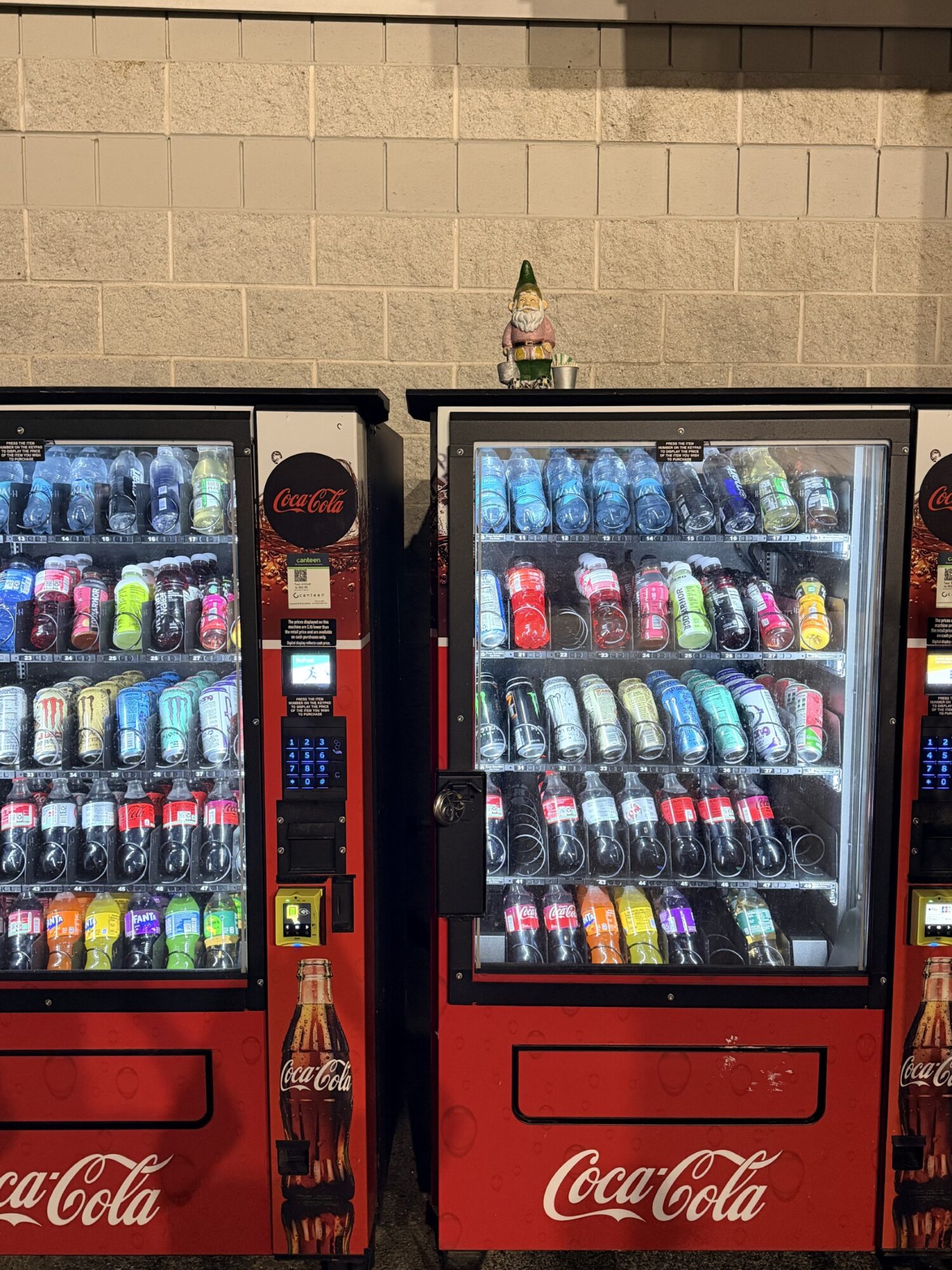 Two vending machines filled with colorful bottled drinks, set against a brick wall background.