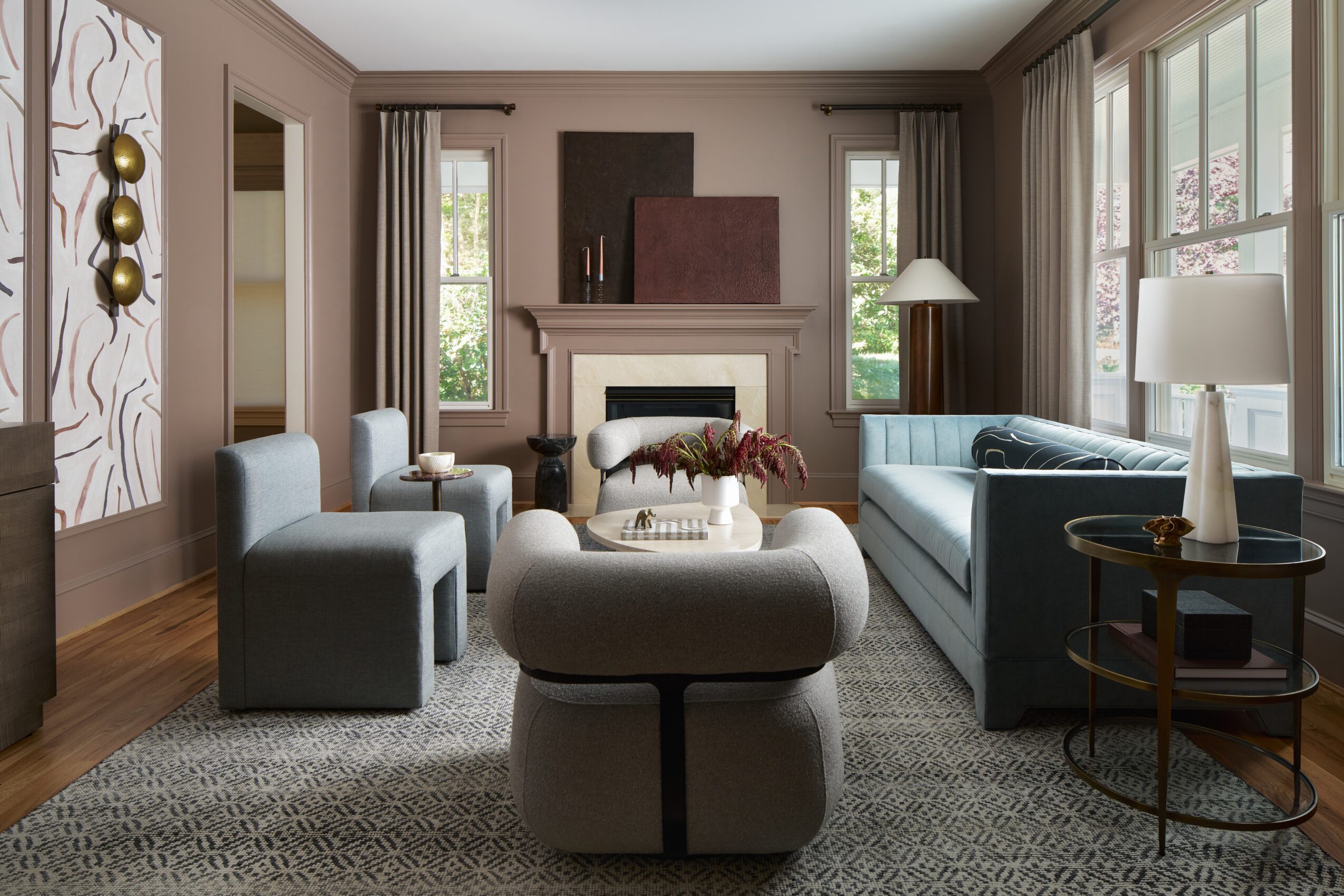 Living room with sofas, armchairs, fireplace, large windows, and decorative wall art, arranged around a central coffee table.