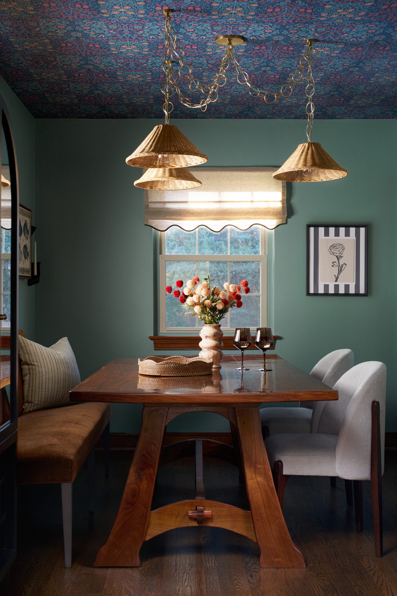 Dining room with a wooden table, chairs, a window with a valance, and hanging pendant lights, decorated with flowers.