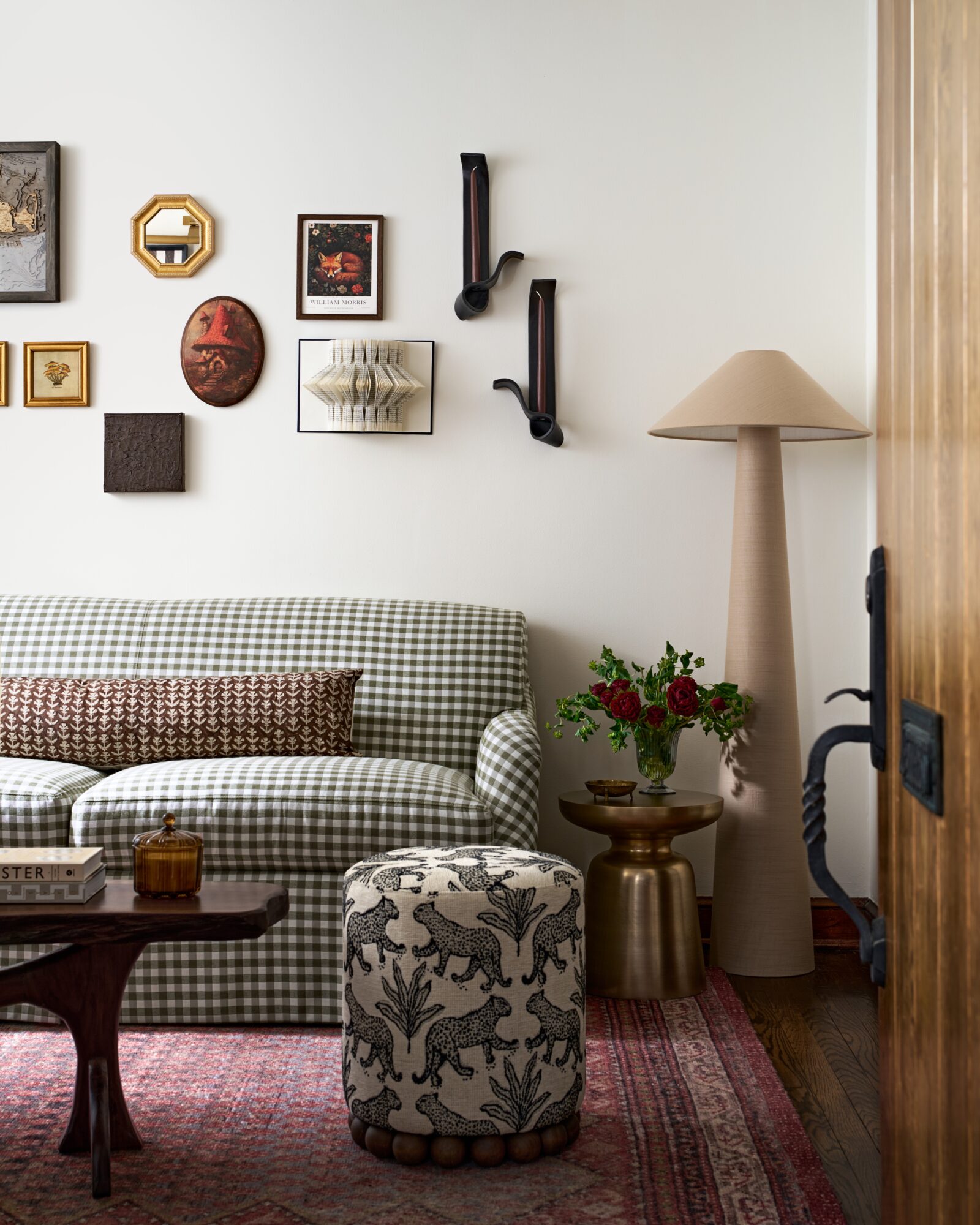Living room with checkered sofa, wall art, a tall lamp, a flower vase, and a patterned ottoman, viewed from the doorway.