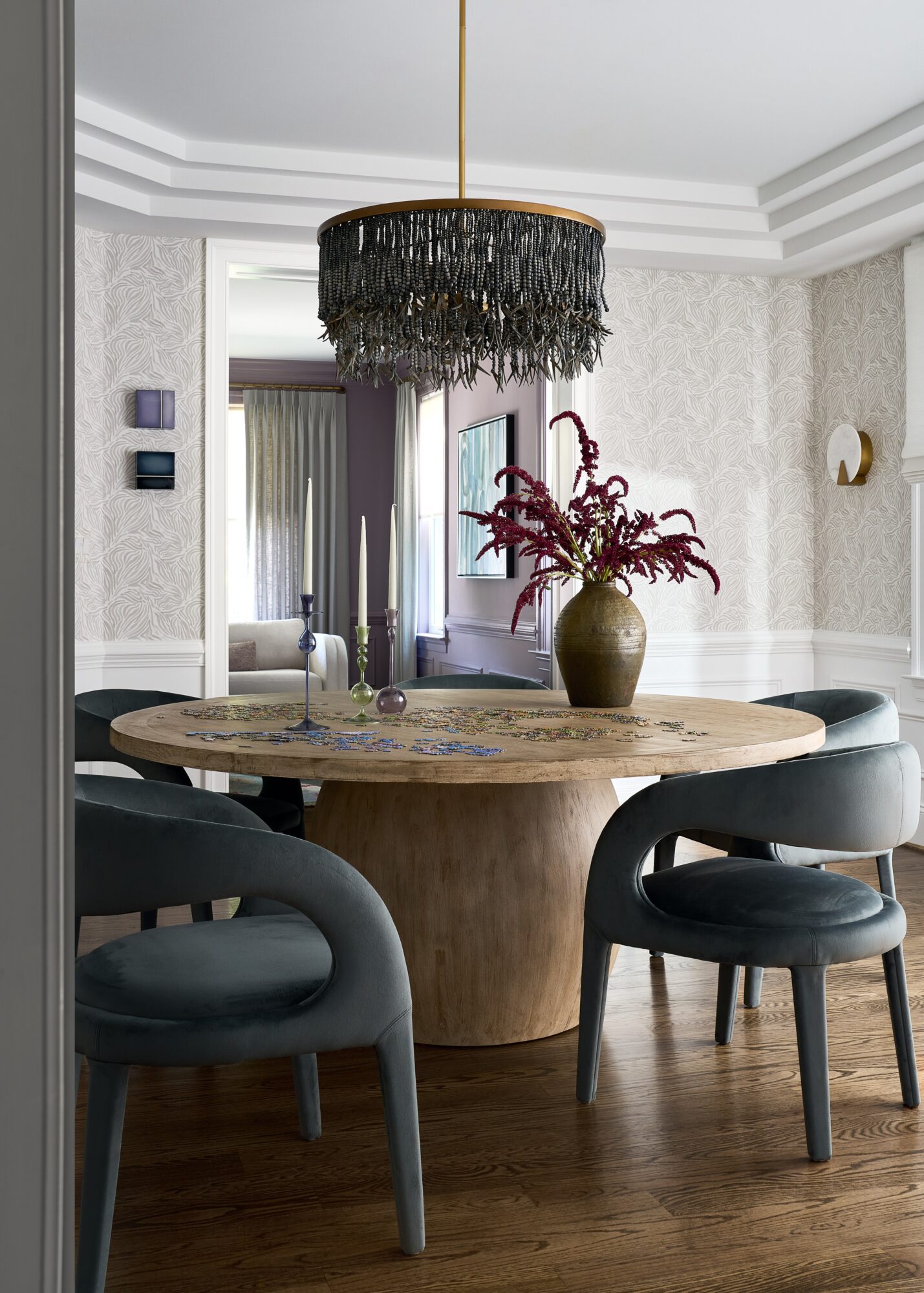 Round dining table with a vase of pink flowers, surrounded by four black chairs, in a modern room with chandelier.