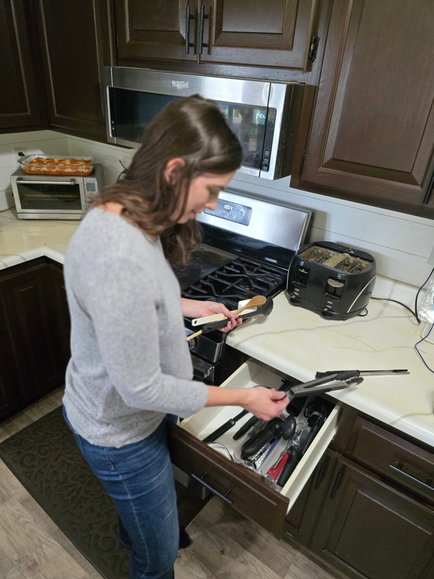 Person opening kitchen oven, with microwave and cabinets visible, in a modern kitchen setting.