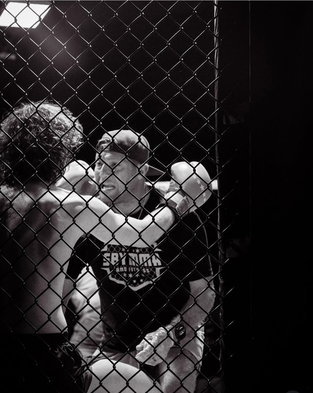 Two fighters in a cage, one with gloves raised, facing each other, with a chain-link fence between them.