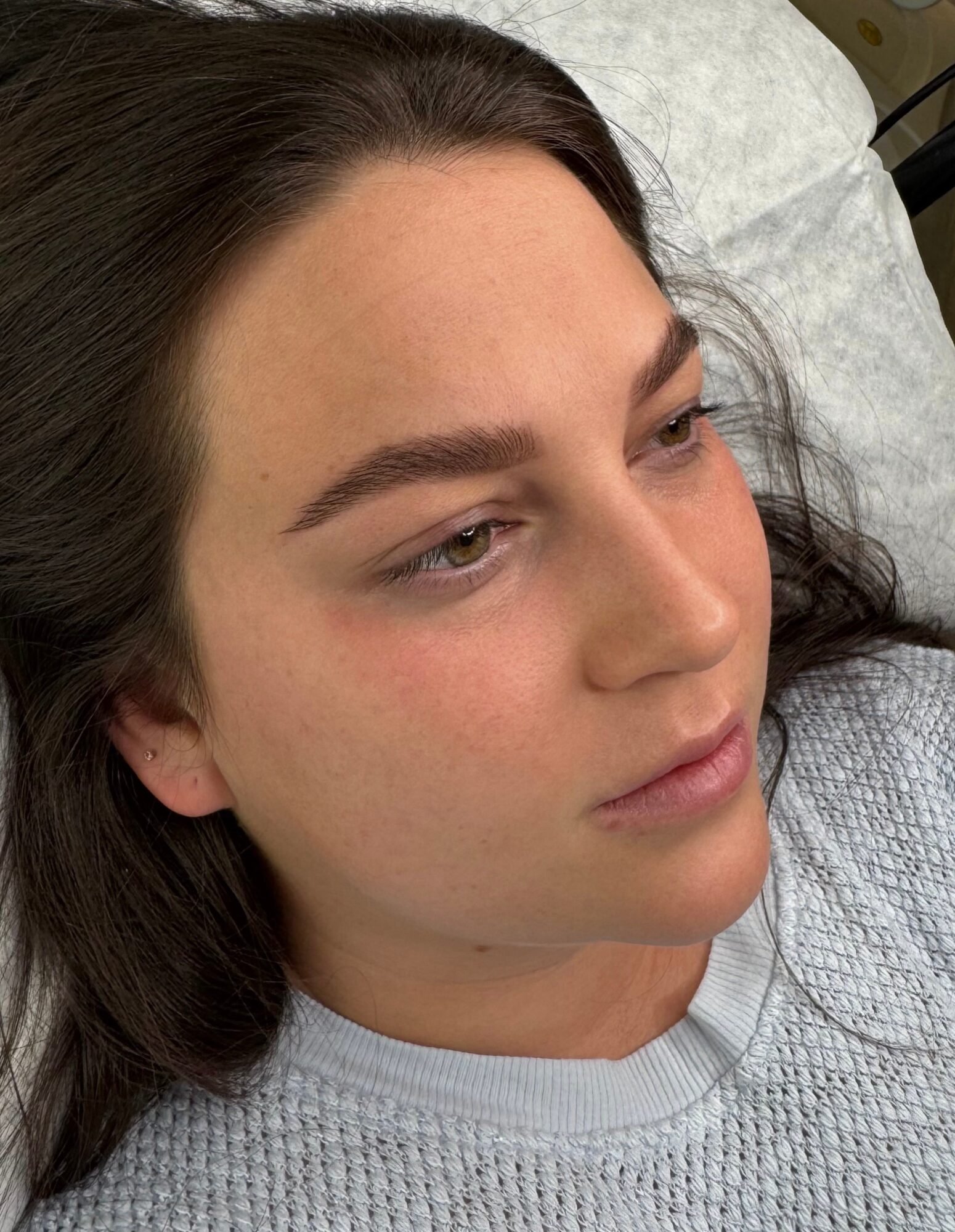Young woman with dark hair lying on a pillow, looking to the side, wearing a light-colored top.