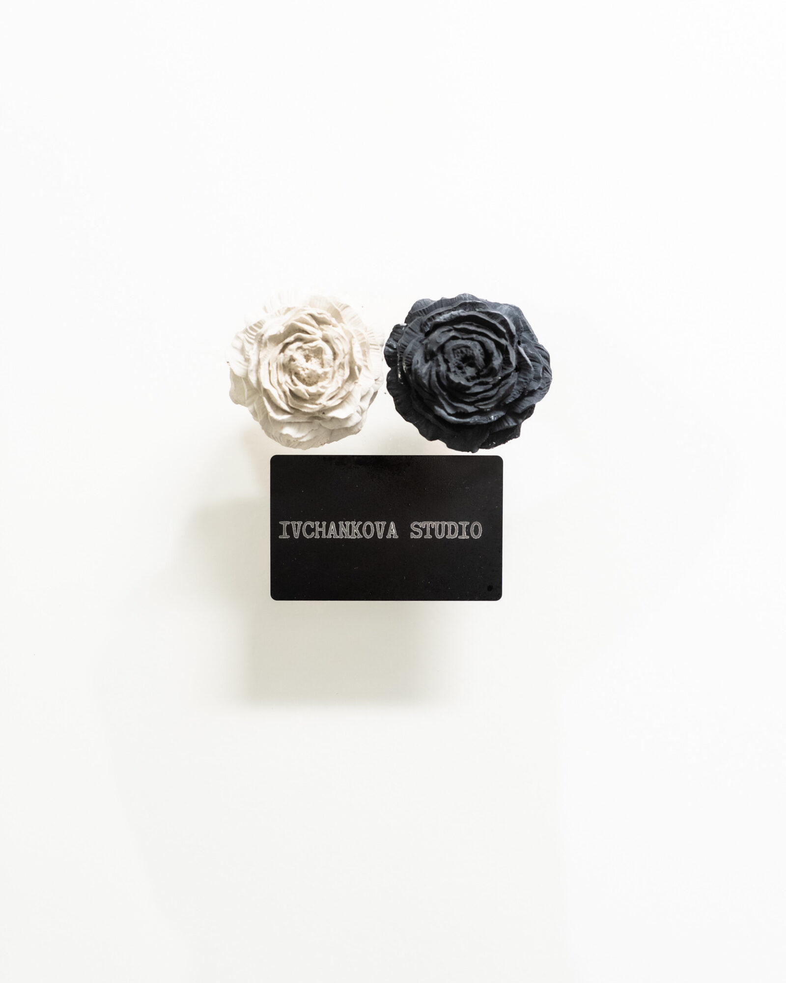 Two fabric flowers, one white and one black, above a black card with white text, on a white background.