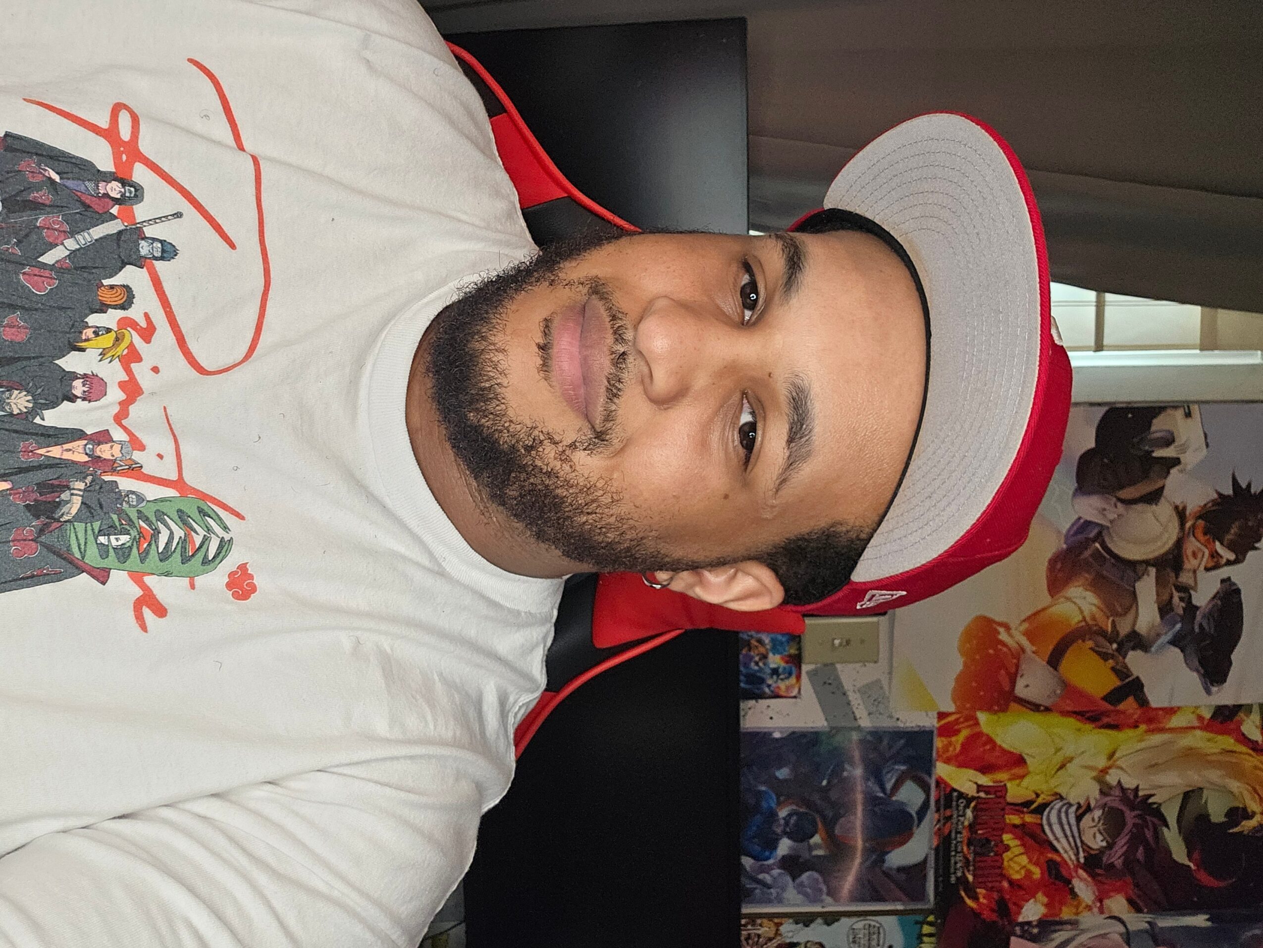 Man with a beard wearing a gray and red cap, sitting indoors with colorful posters in the background.