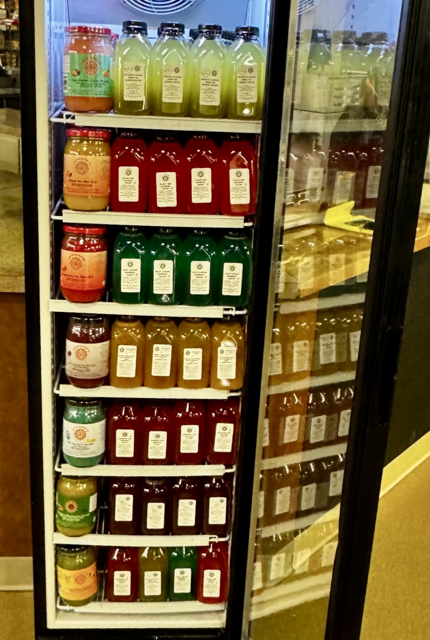 Refrigerator with shelves of bottled beverages in various colors, including green, red, yellow, and brown, with a glass door on the right.