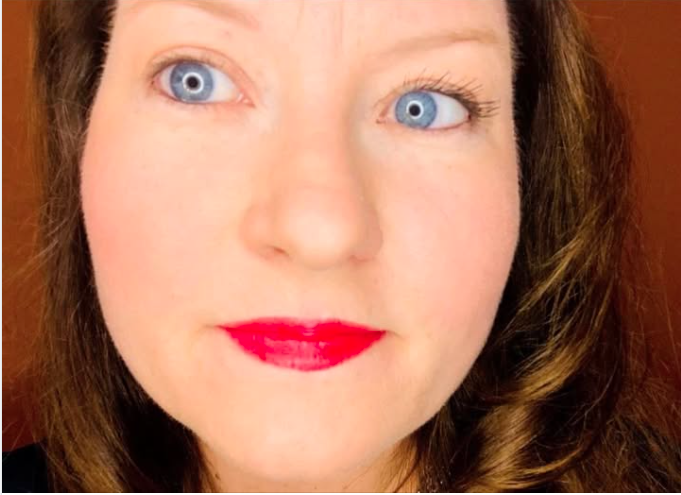 Close-up of a woman with blue eyes, red lipstick, and brown hair, looking slightly to the side.