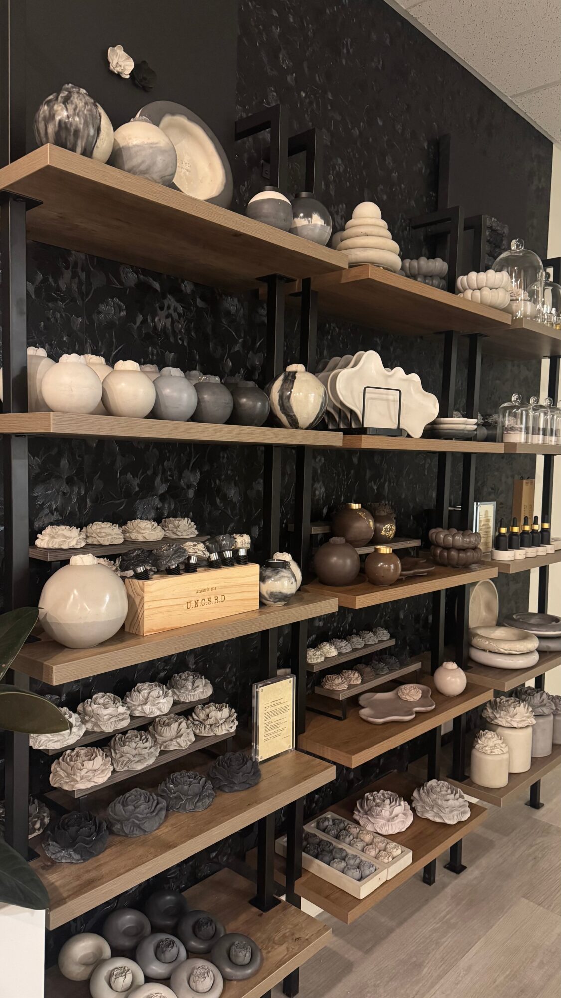 Shelves filled with various ceramic and decorative objects, including bowls, vases, and sculptures, arranged on wooden shelves against a dark wall.