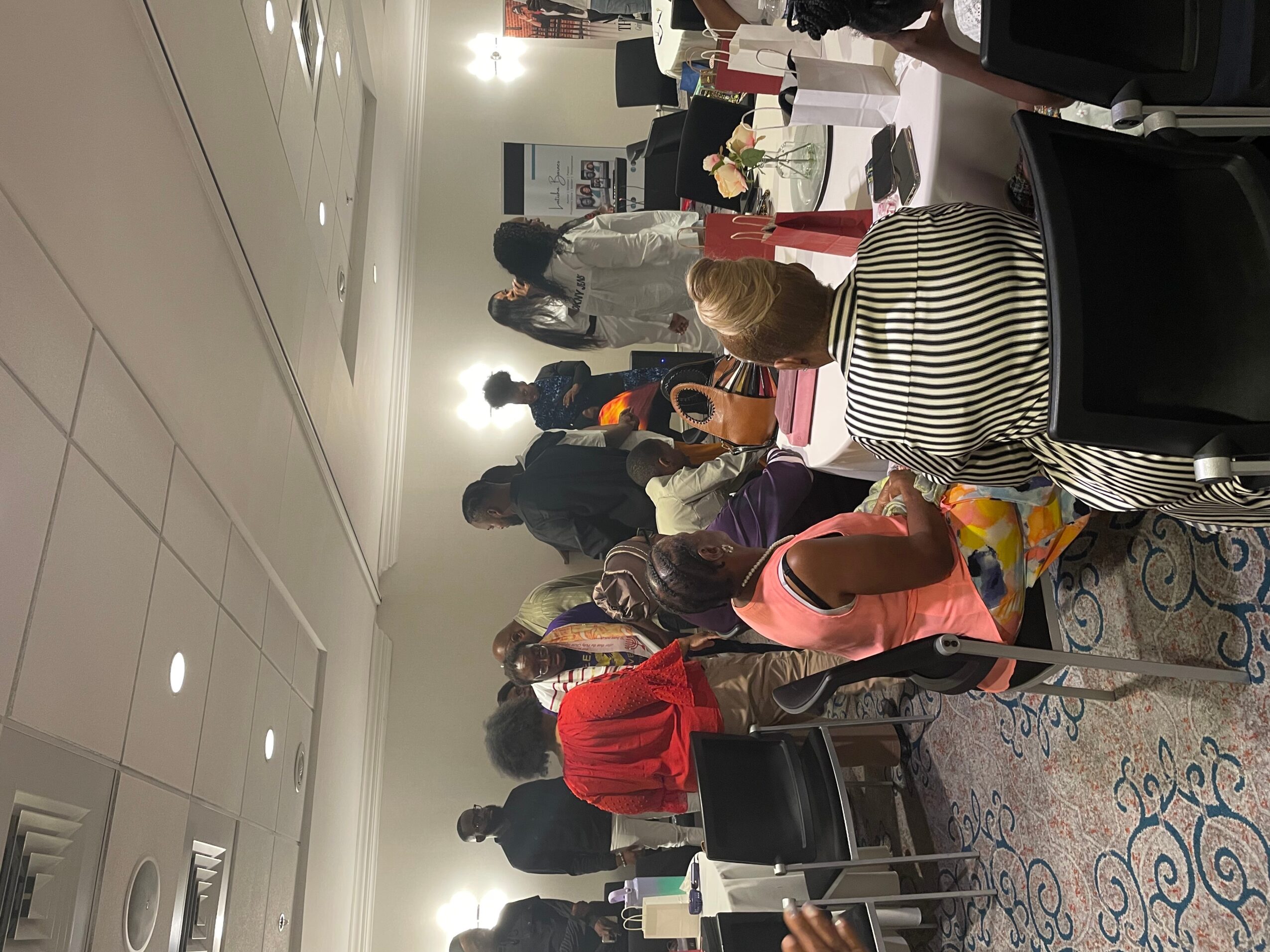 People gathered around tables in a room with white walls and ceiling, some standing and some sitting, engaging in conversation.