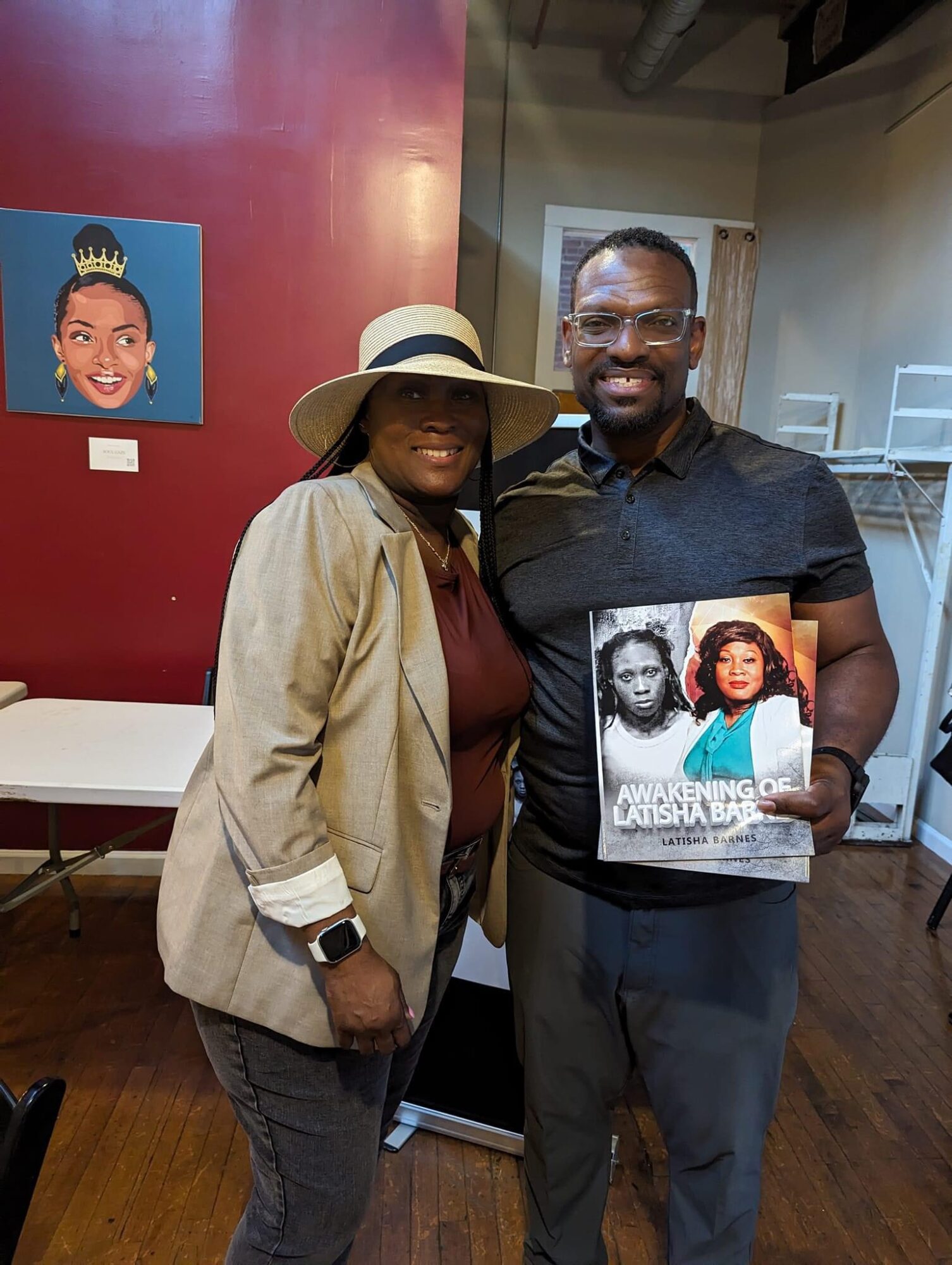 Two people standing indoors, one holding a magazine with a woman on the cover, smiling at the camera.