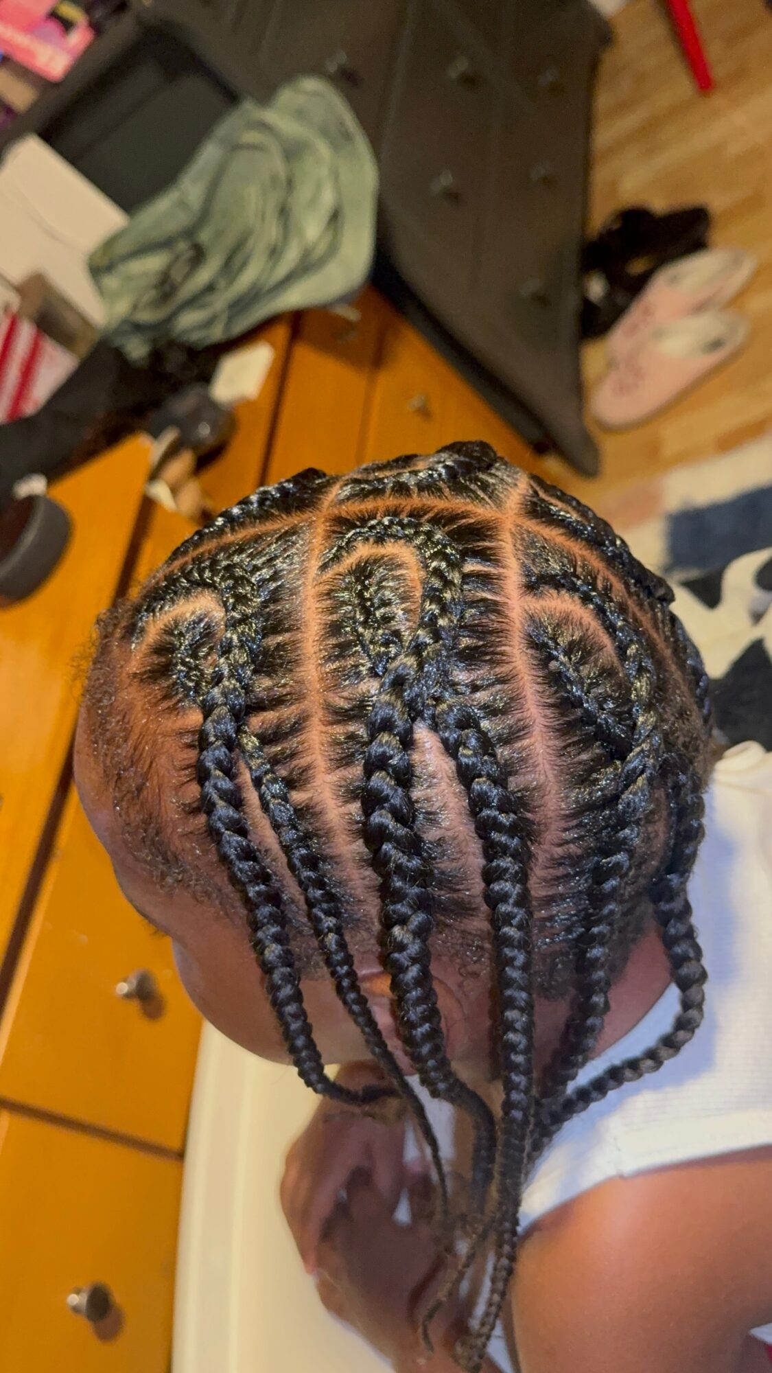 Top view of a person's head with braided hair styled in multiple sections, some with beads, on a wooden surface.